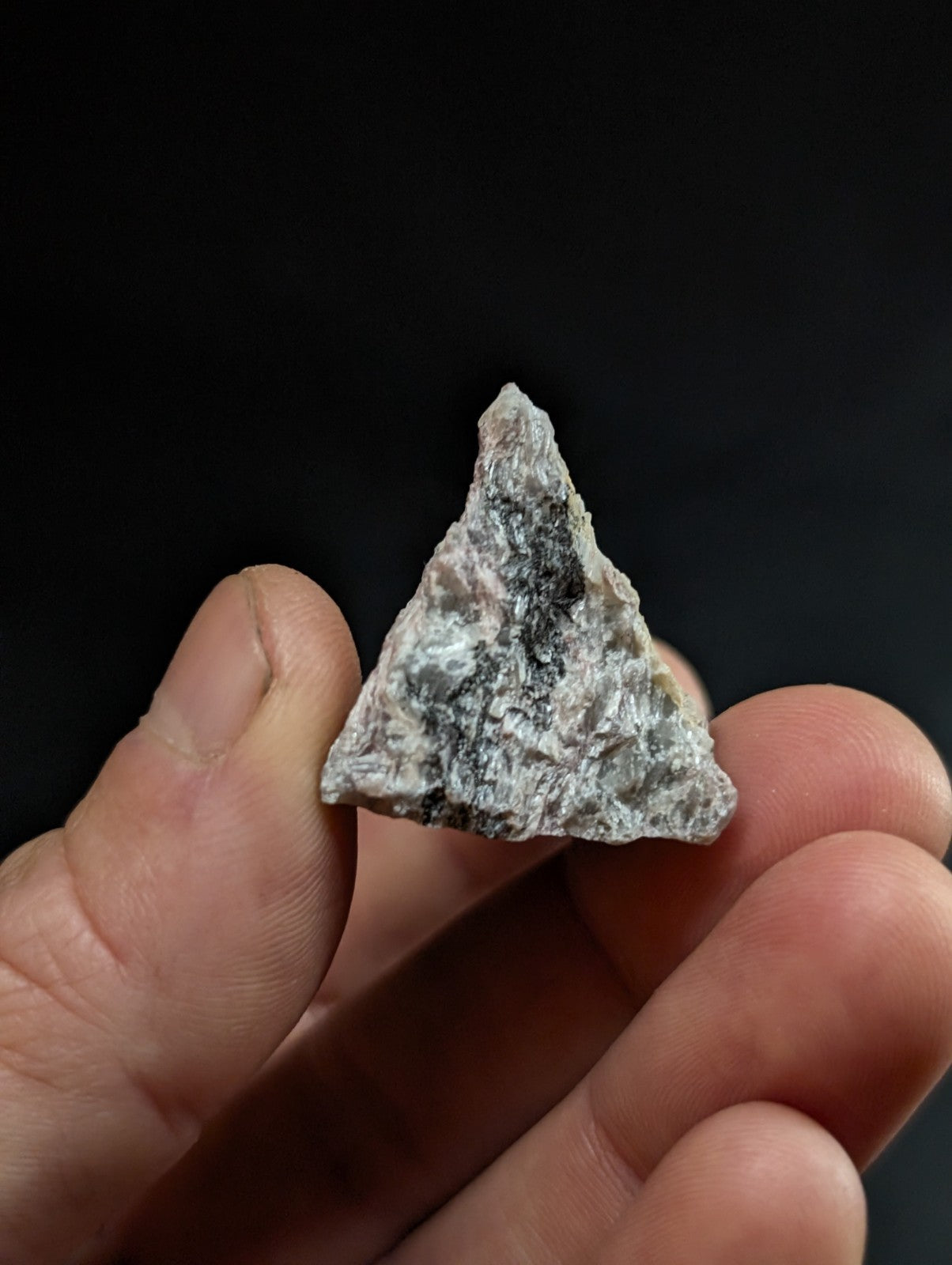 A triangular, rough-textured mineral specimen with a mottled gray and white surface.