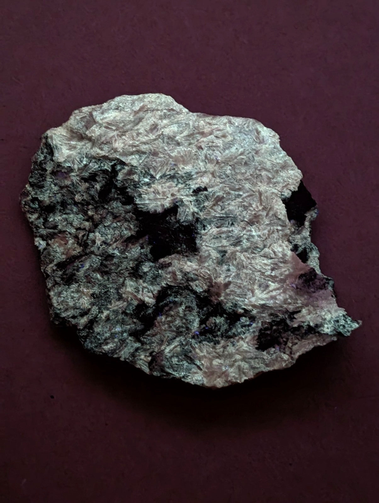 A rough, irregularly shaped mineral specimen with a mottled surface of gray, black, and subtle pinkish hues.