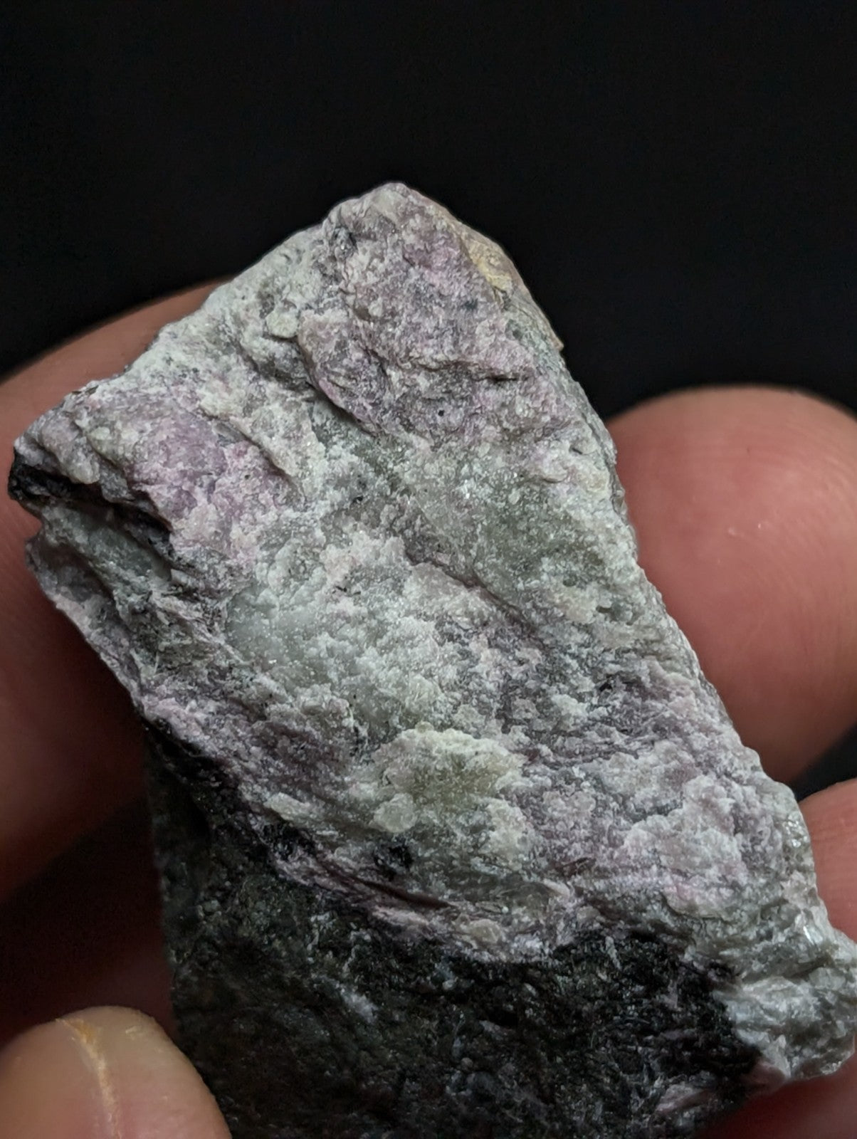 A rough, irregularly shaped stone with a mottled surface of gray, greenish hues and subtle purple undertones.