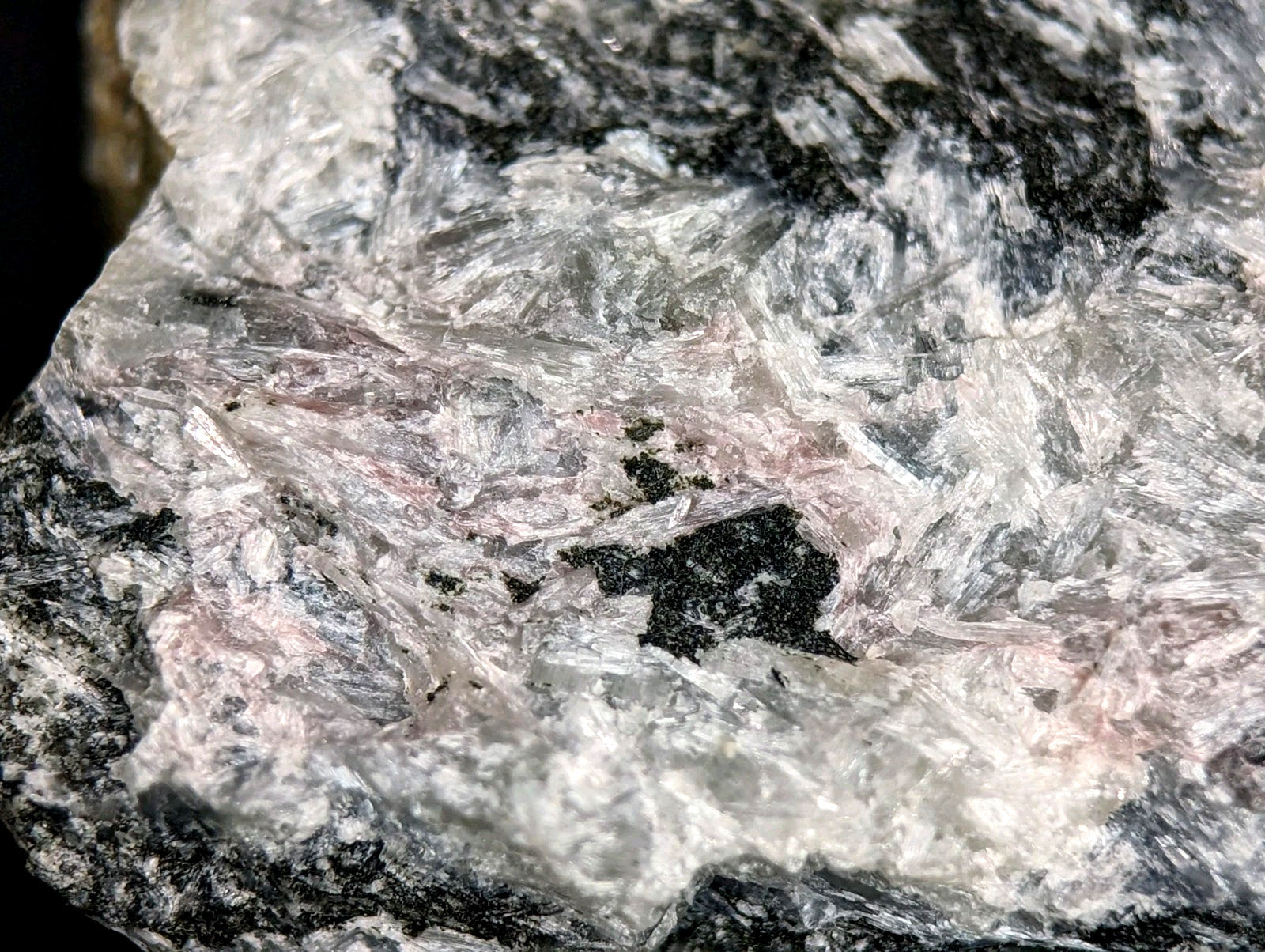 A translucent, crystalline mineral specimen with a mix of white and pinkish hues interwoven through dark gray to black matrix.