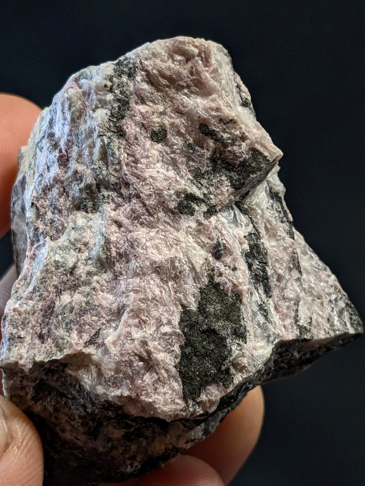 A rough, irregularly shaped pinkish-gray rock with dark green and black mineral inclusions.
