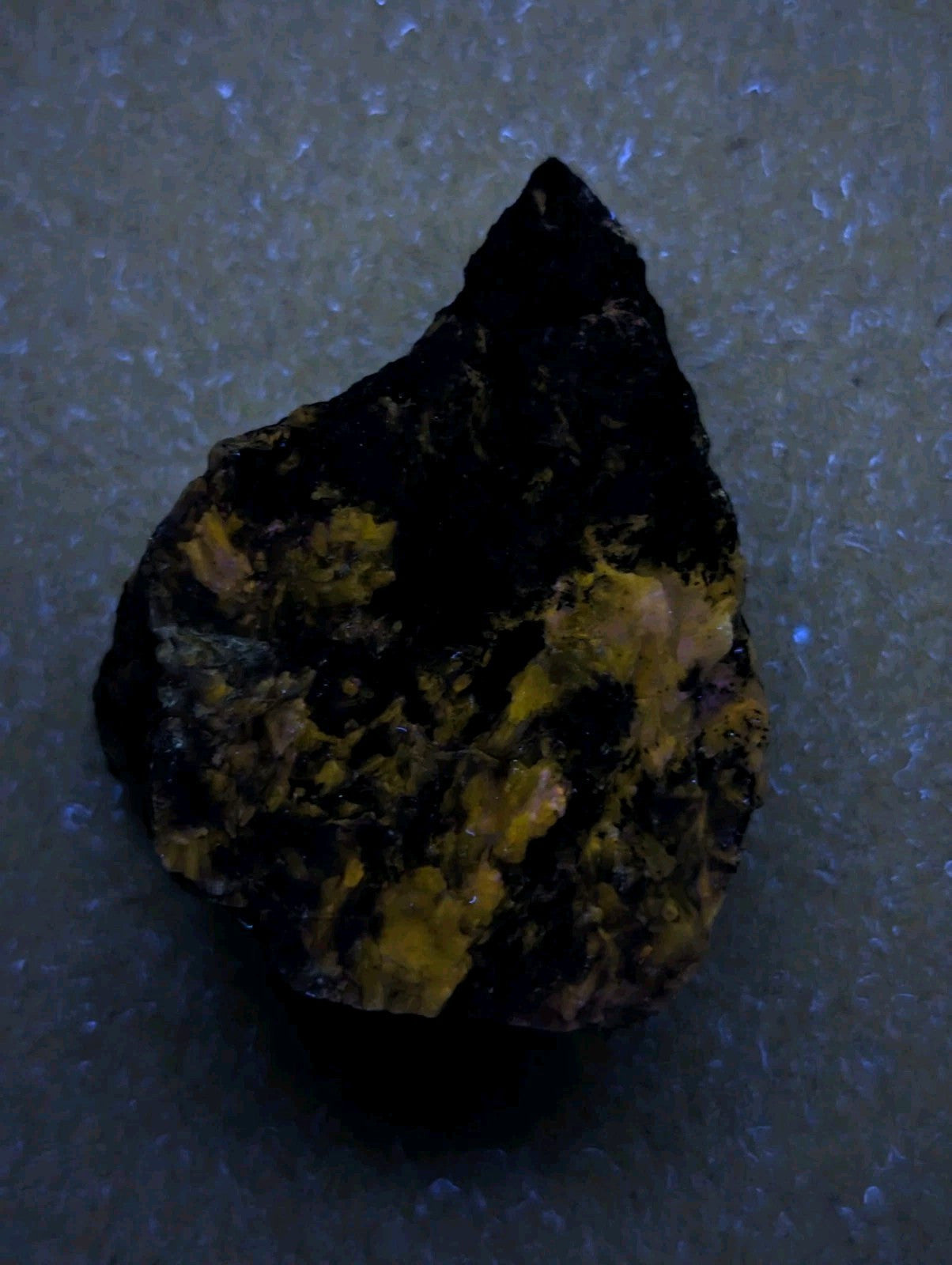 A dark, irregularly shaped rock with patches of bright yellow mineral inclusions.