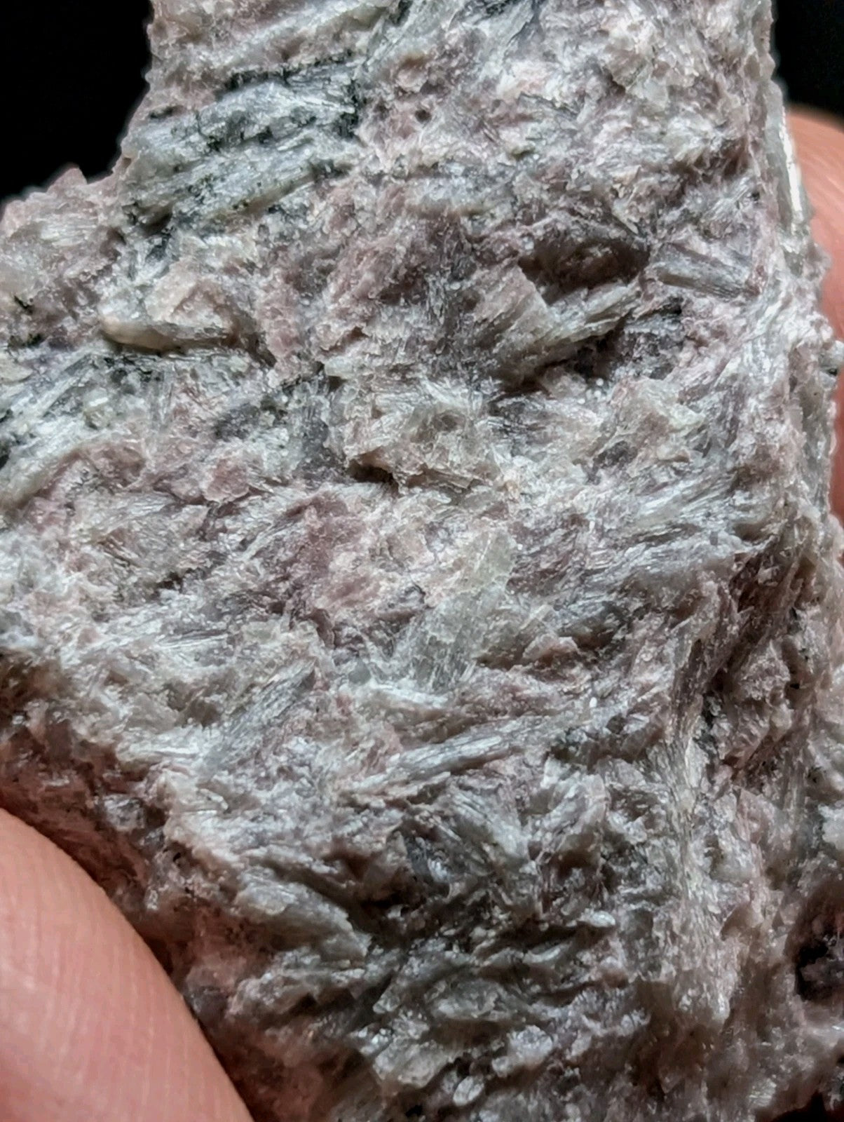 A rough, grayish-green mineral specimen with a fibrous texture and visible crystalline structures.