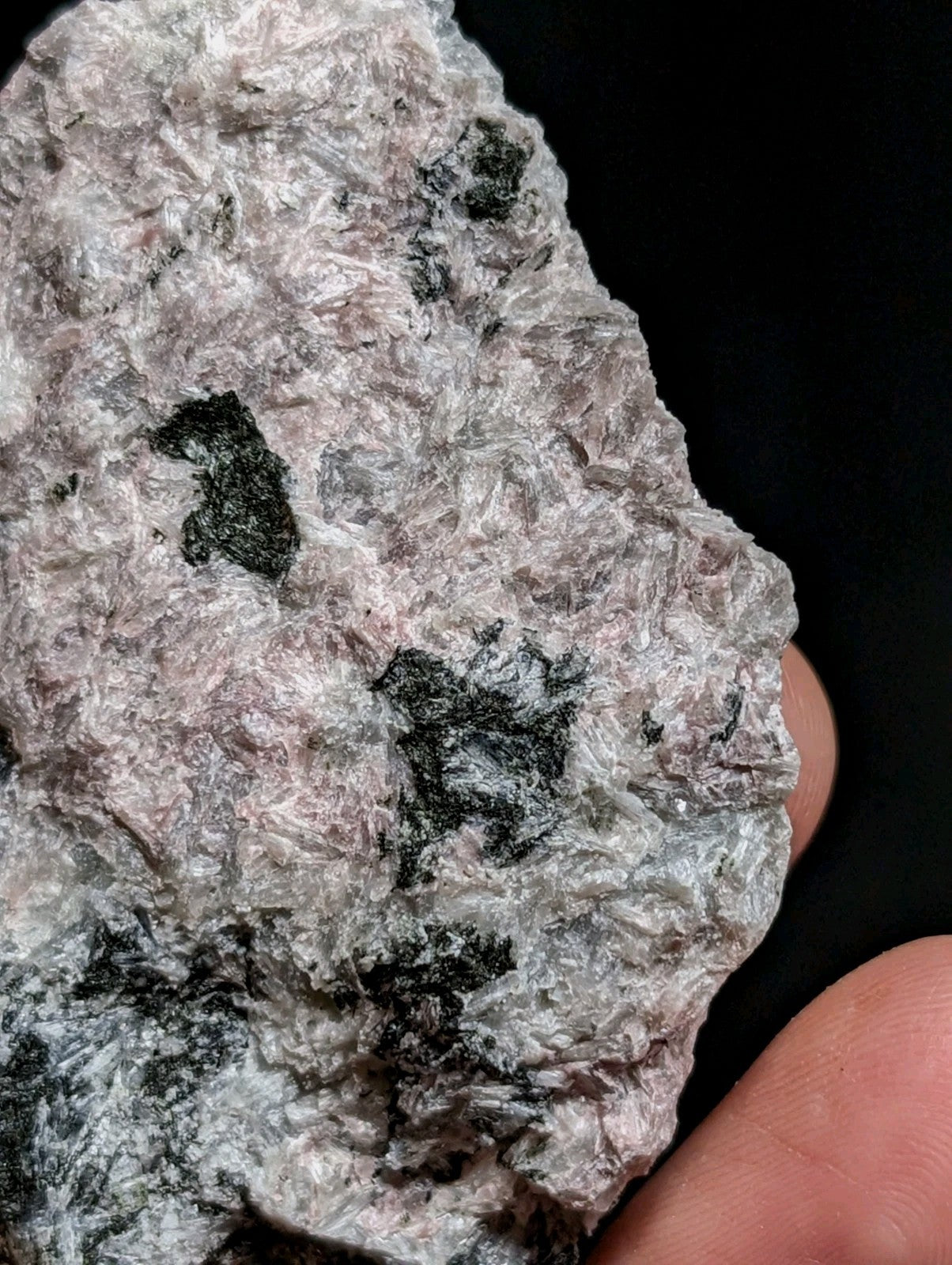 A rough, irregularly shaped mineral specimen with a textured surface displaying patches of pale pink and grayish-white hues interspersed with dark black inclusions.