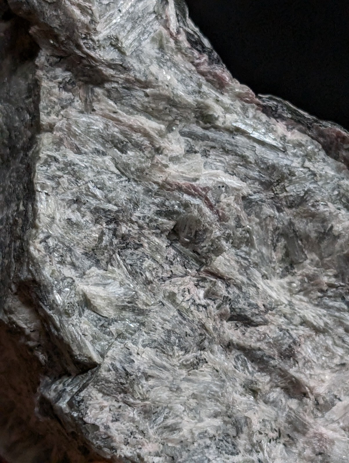 A rugged, grayish-white rock with a fibrous texture and subtle pinkish streaks.