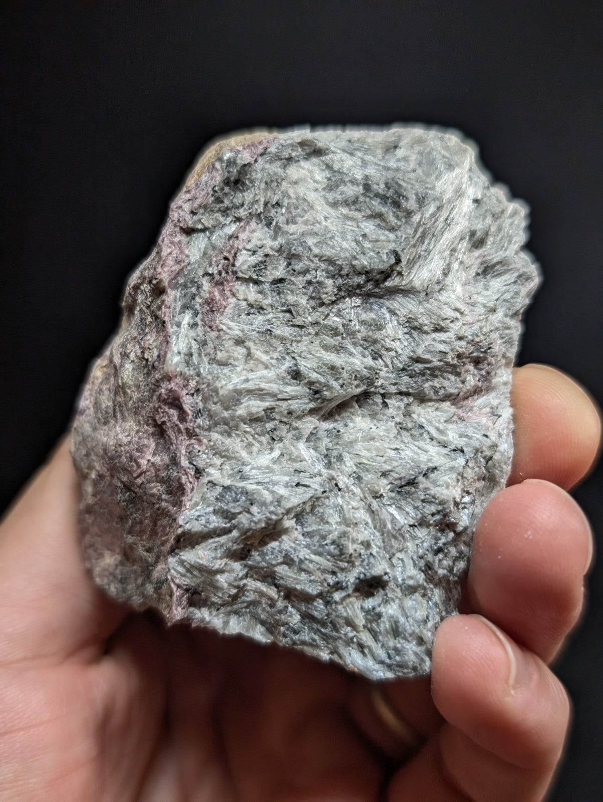 A rough, irregularly shaped mineral specimen with a textured surface displaying shades of gray and subtle pinkish hues.