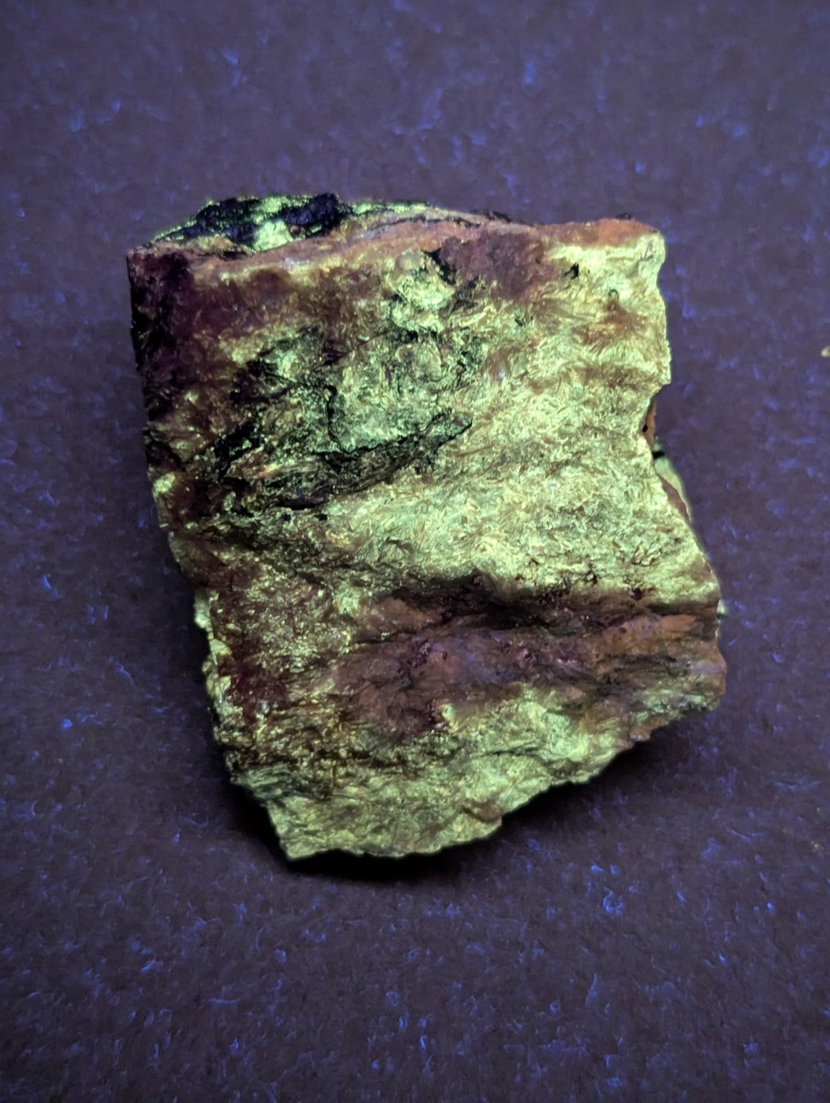 A rough, irregularly shaped mineral specimen with a mottled surface of greenish-yellow and reddish-brown hues.