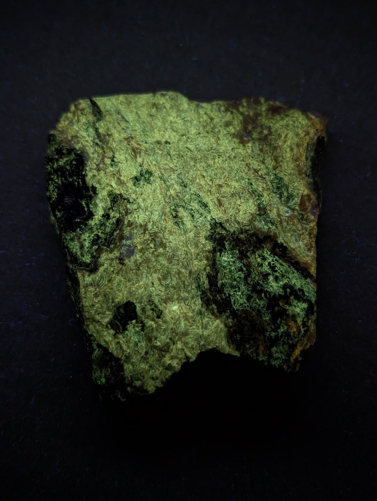 A rough, irregularly shaped piece of green mineral with patches of dark veining and a textured surface.