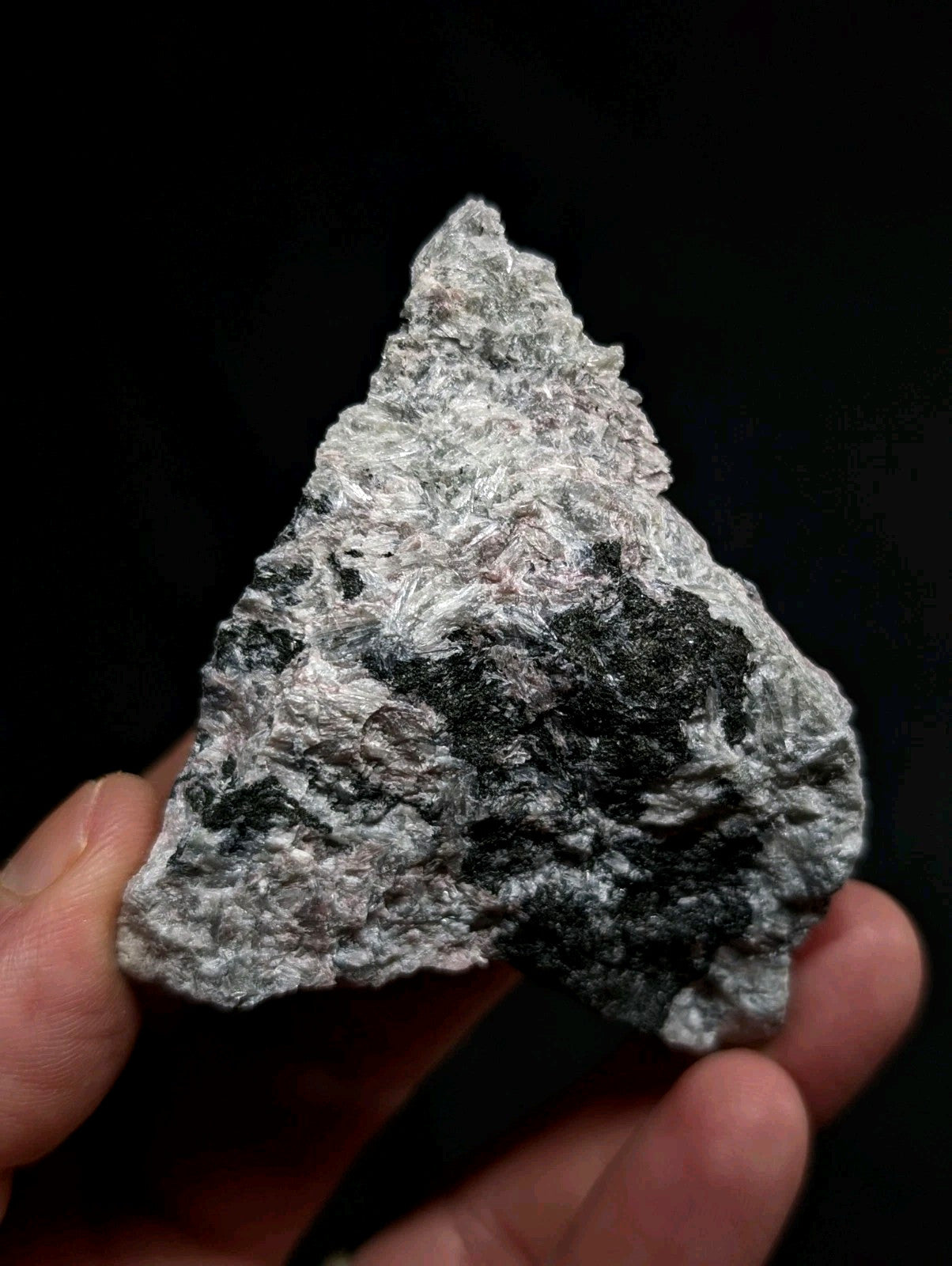 A triangular, rough-textured mineral specimen with a mottled pattern of silver-gray and dark black patches.