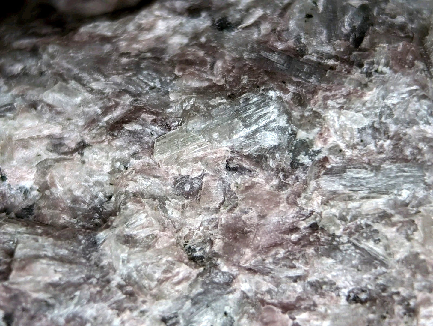 A rough, textured rock surface with a mottled pattern of gray, white, and subtle pinkish hues.