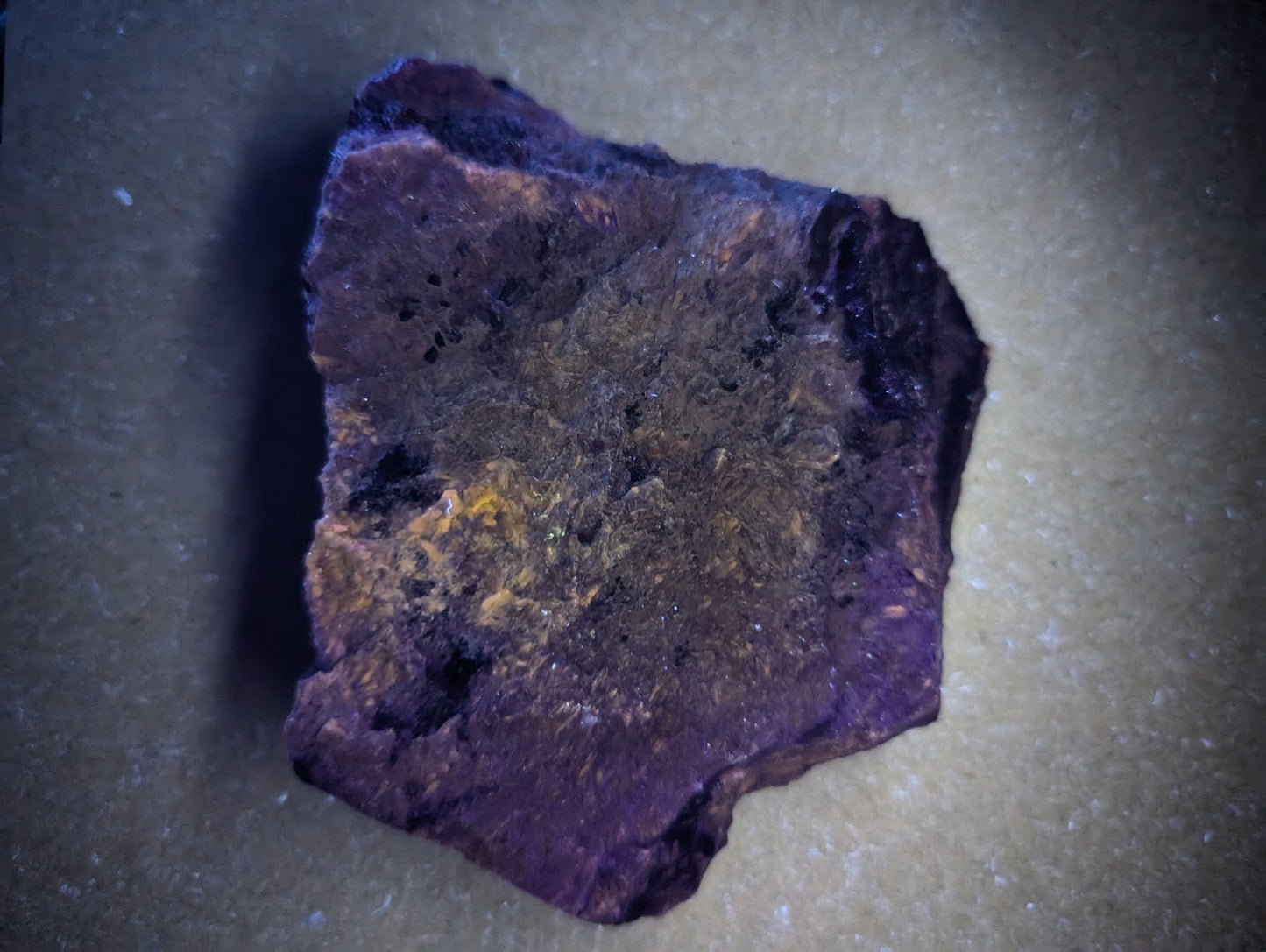 A rough, irregularly shaped purple mineral specimen with patches of brown and yellowish discoloration.