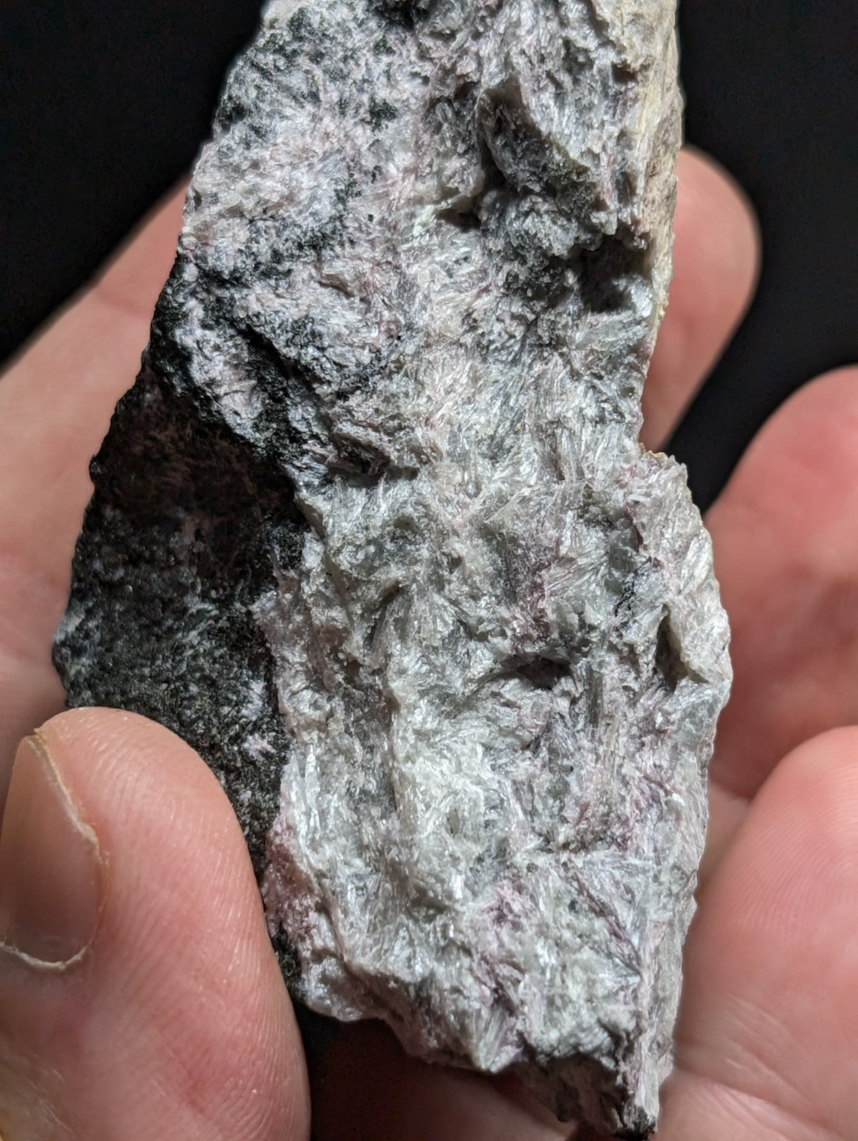 A rough, irregularly shaped mineral specimen with a mottled gray and black surface featuring fibrous textures.