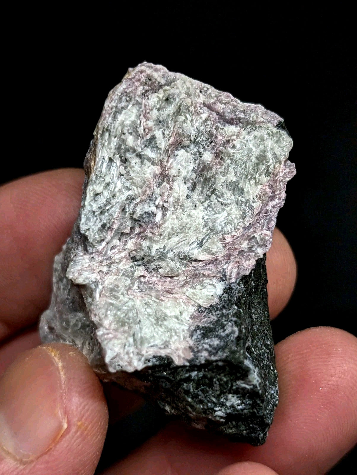 A rough, irregularly shaped mineral specimen with a mottled surface of white and pale pink hues against a dark base.