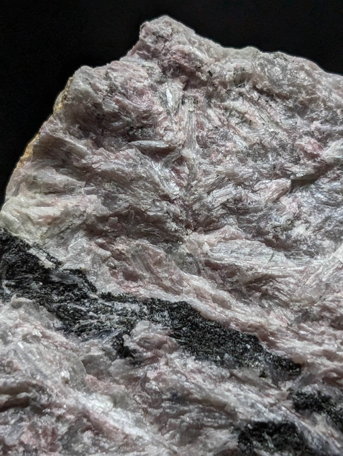 A rough, naturally occurring mineral specimen with a textured surface displaying shades of pale pink and white, accented by dark black streaks.