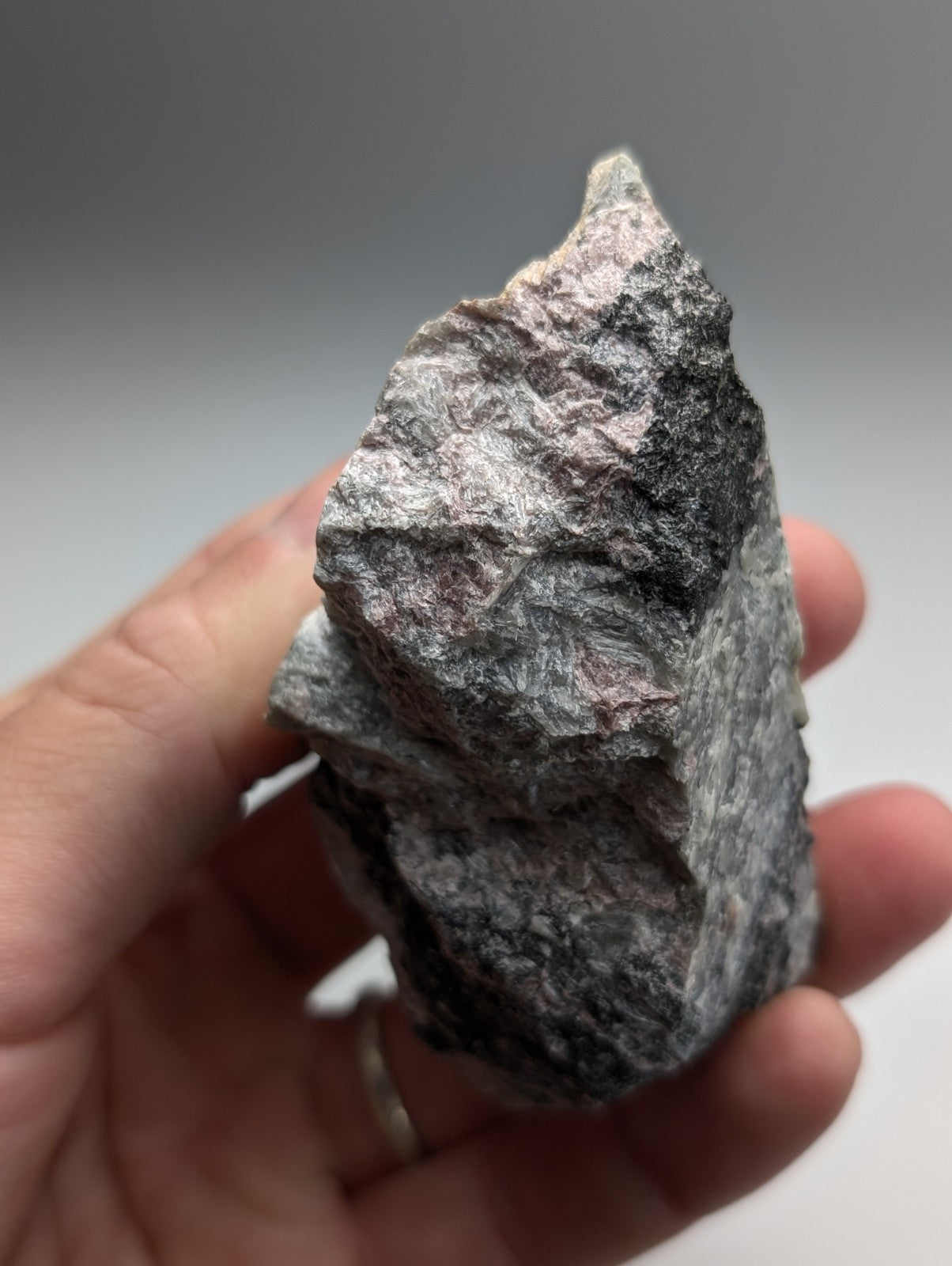 A rugged irregular miserite and wollastonite rock with gray and subtle pink hues from wilson springs arkansas held in hand