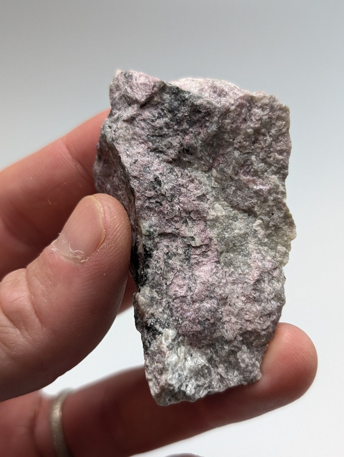 A rough, irregularly shaped piece of pinkish-gray rock with speckled black and white mineral inclusions.