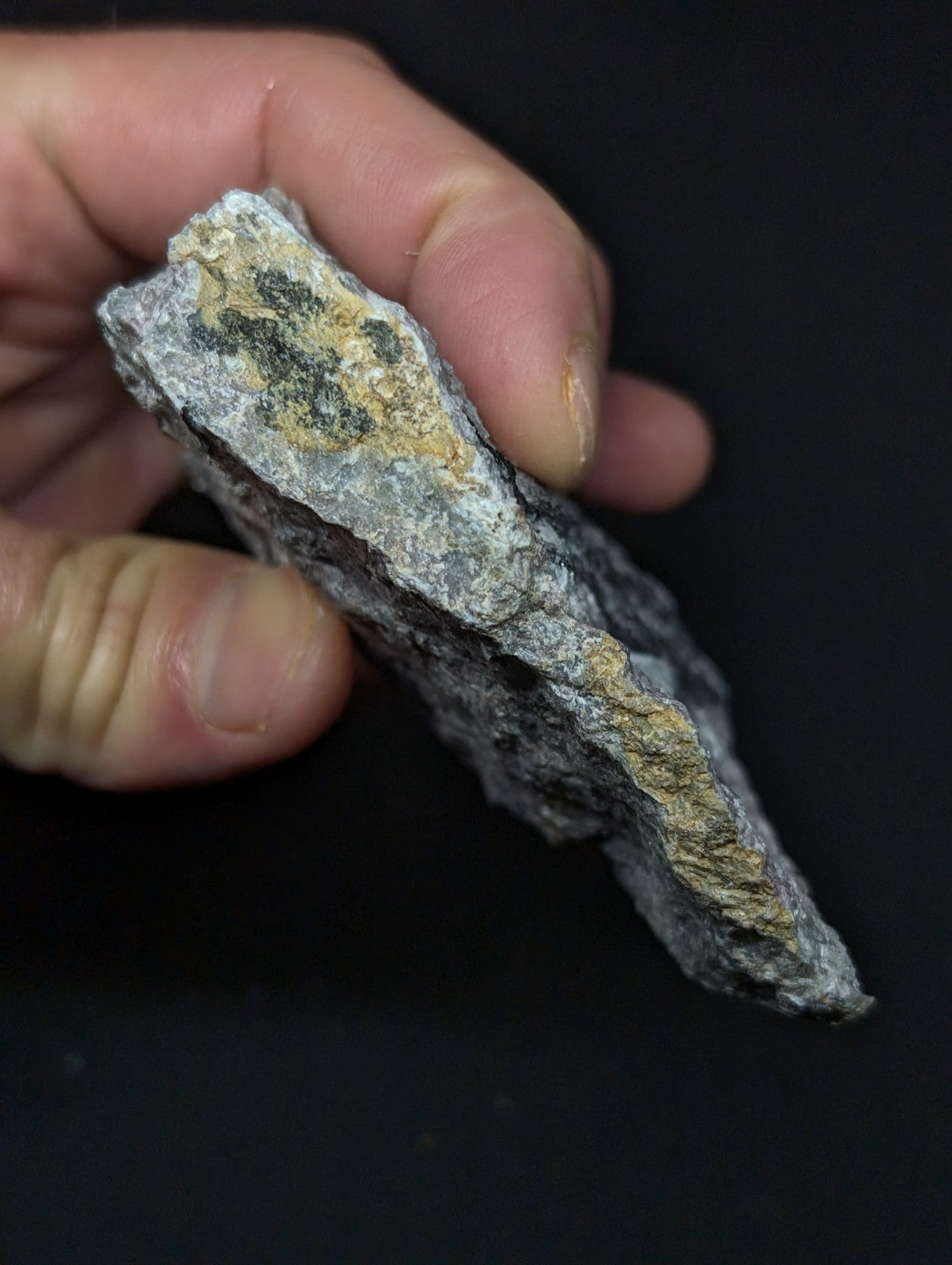 A rough, irregularly shaped rock with a gray base and patches of yellowish-brown mineral streaks.