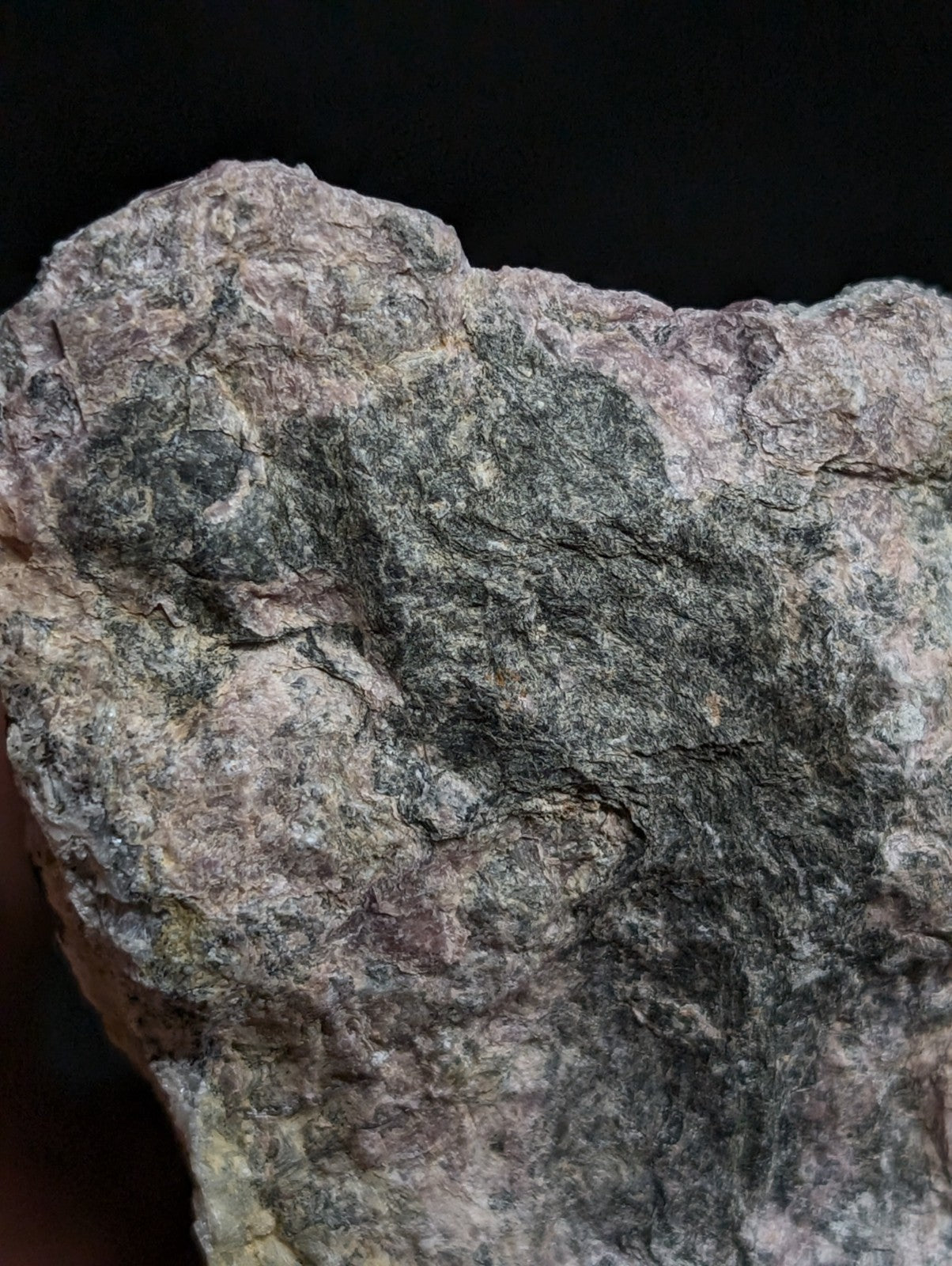 A rugged, naturally textured rock with a mottled pattern of gray and pinkish hues.