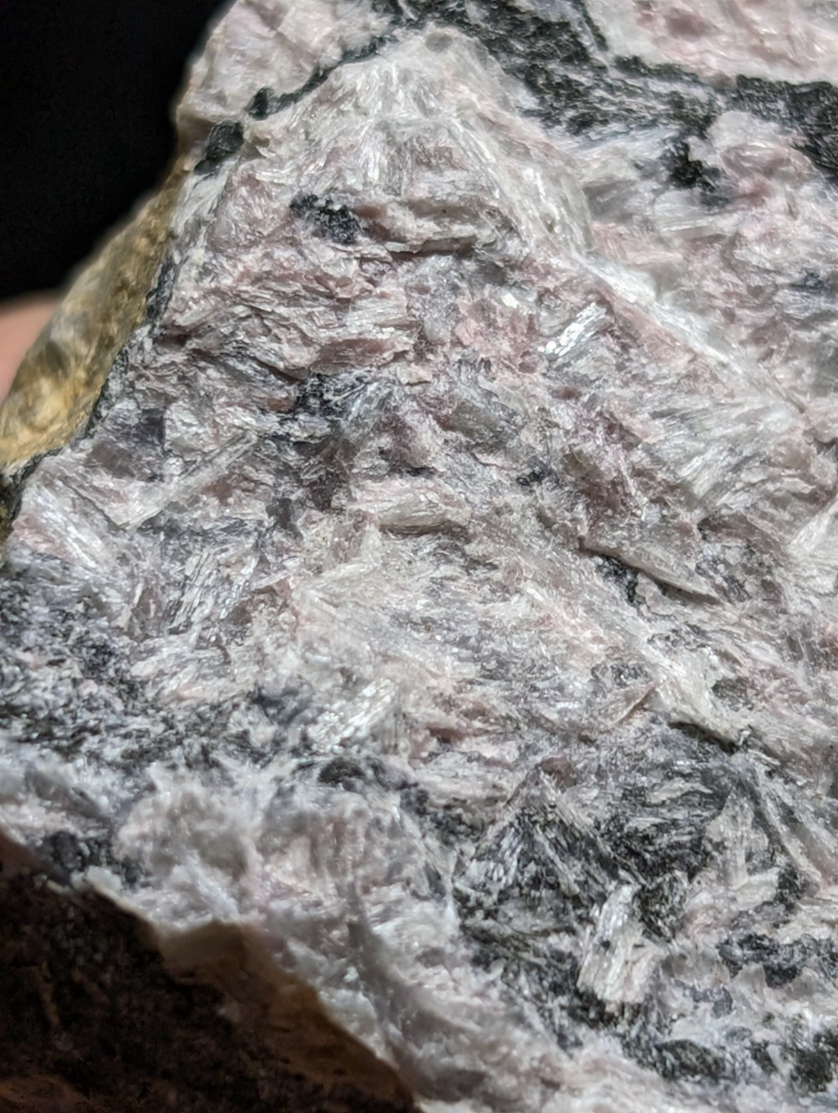 A rough, naturally occurring mineral specimen with a mottled surface of white and gray crystalline textures interspersed with dark streaks.