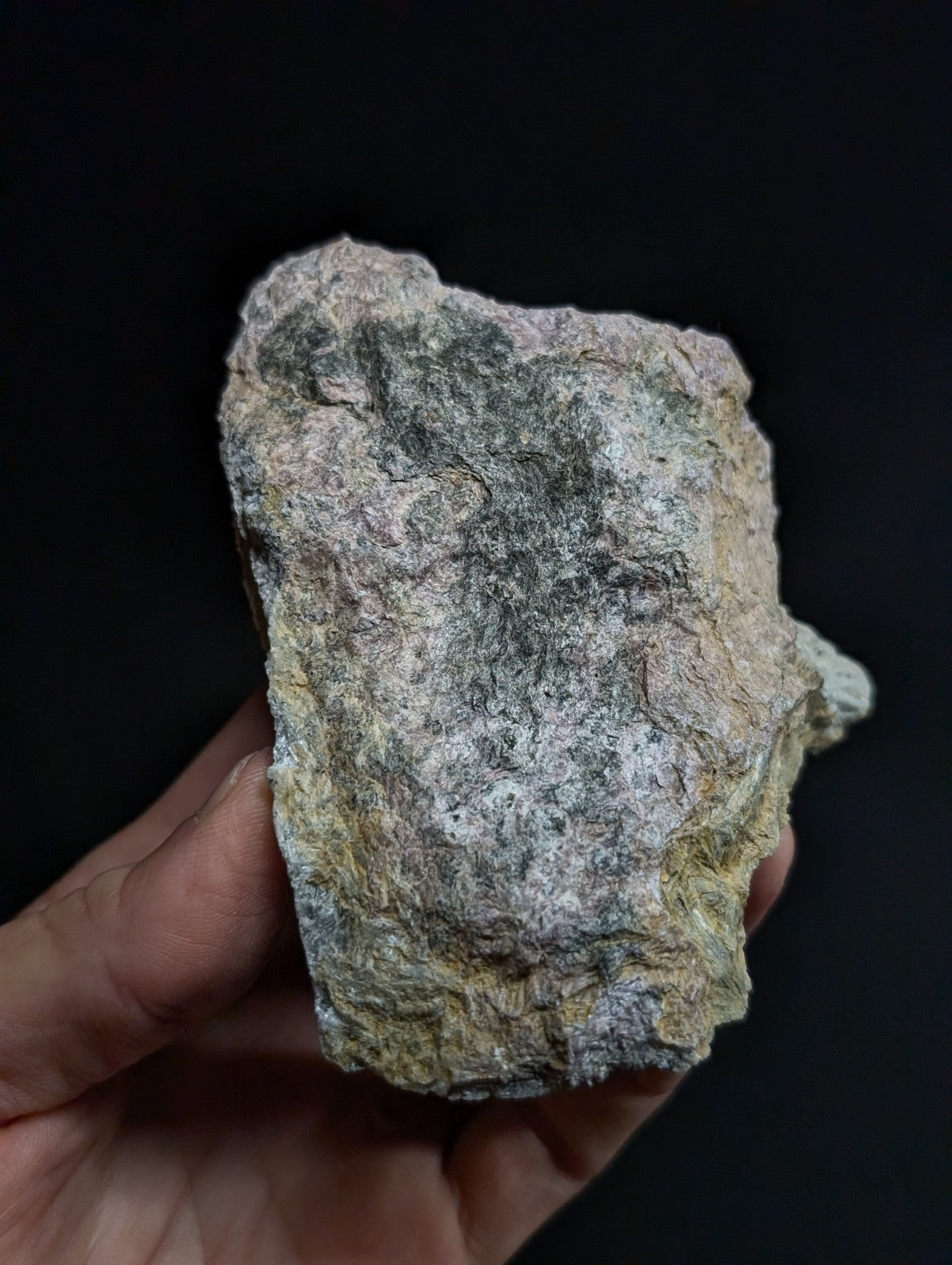 A rough, irregularly shaped stone with a mottled surface of gray, greenish-gray, and faint yellow tones.