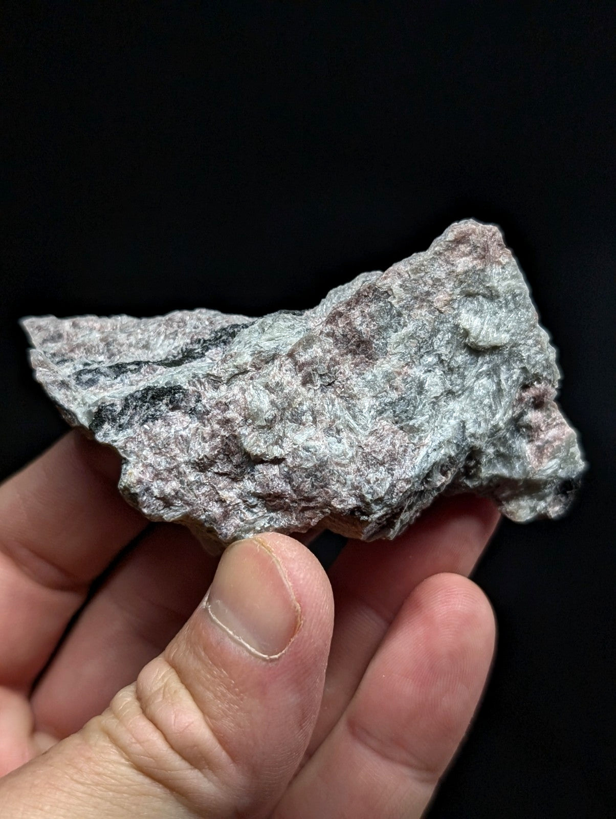 A rough, irregularly shaped rock with a mottled gray and pinkish surface held in someone’s hand.