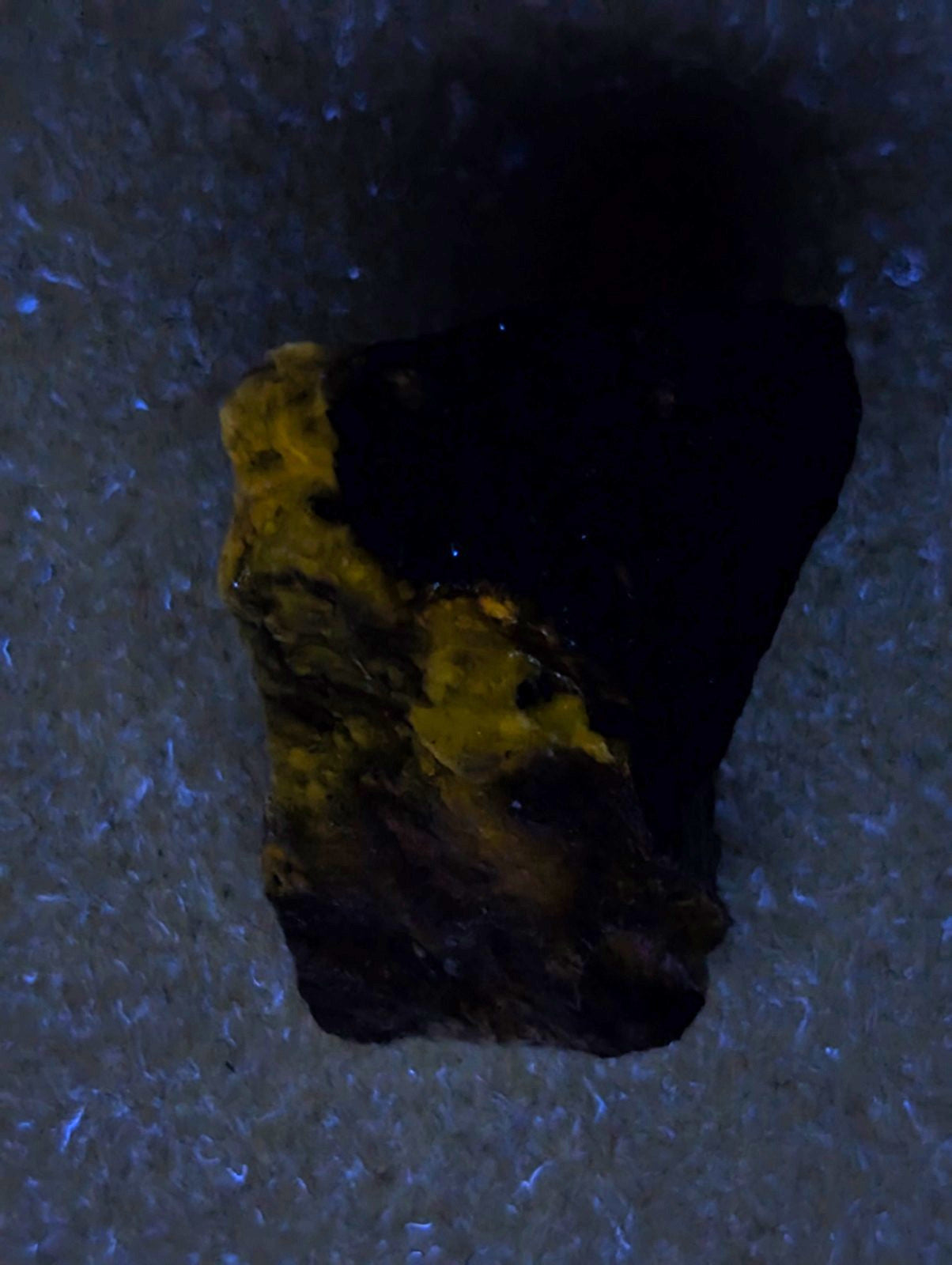 A rough, irregularly shaped piece of ore with a dark base and patches of bright yellow mineral.