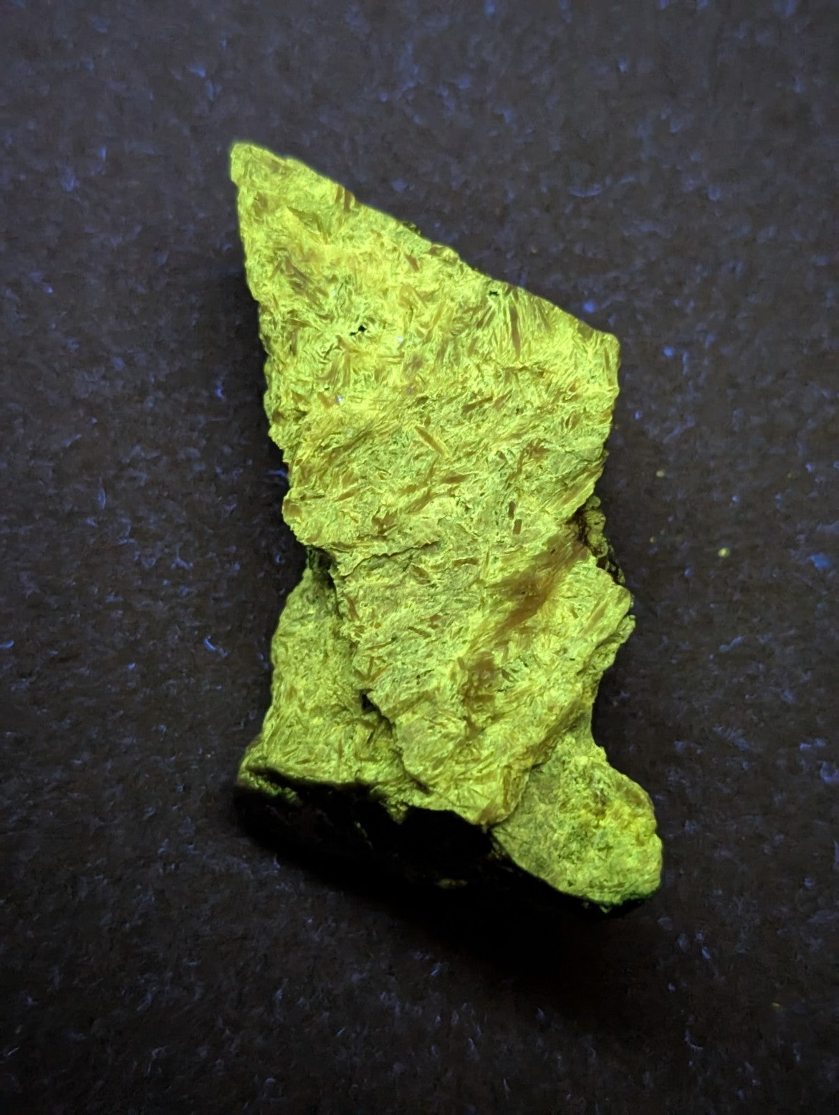 A rough, irregularly shaped piece of bright green mineral with a textured surface.