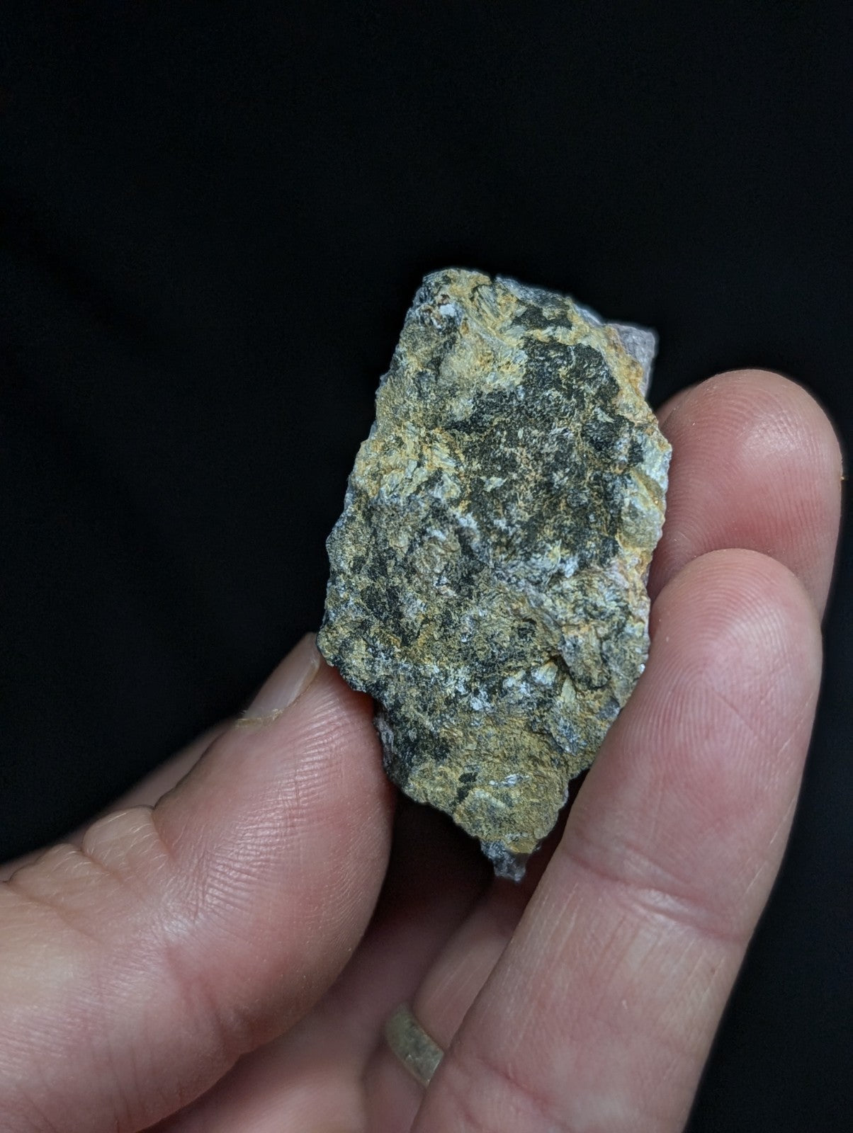A rough, irregularly shaped mineral specimen with a mottled green and gray surface held gently in someone’s hand.