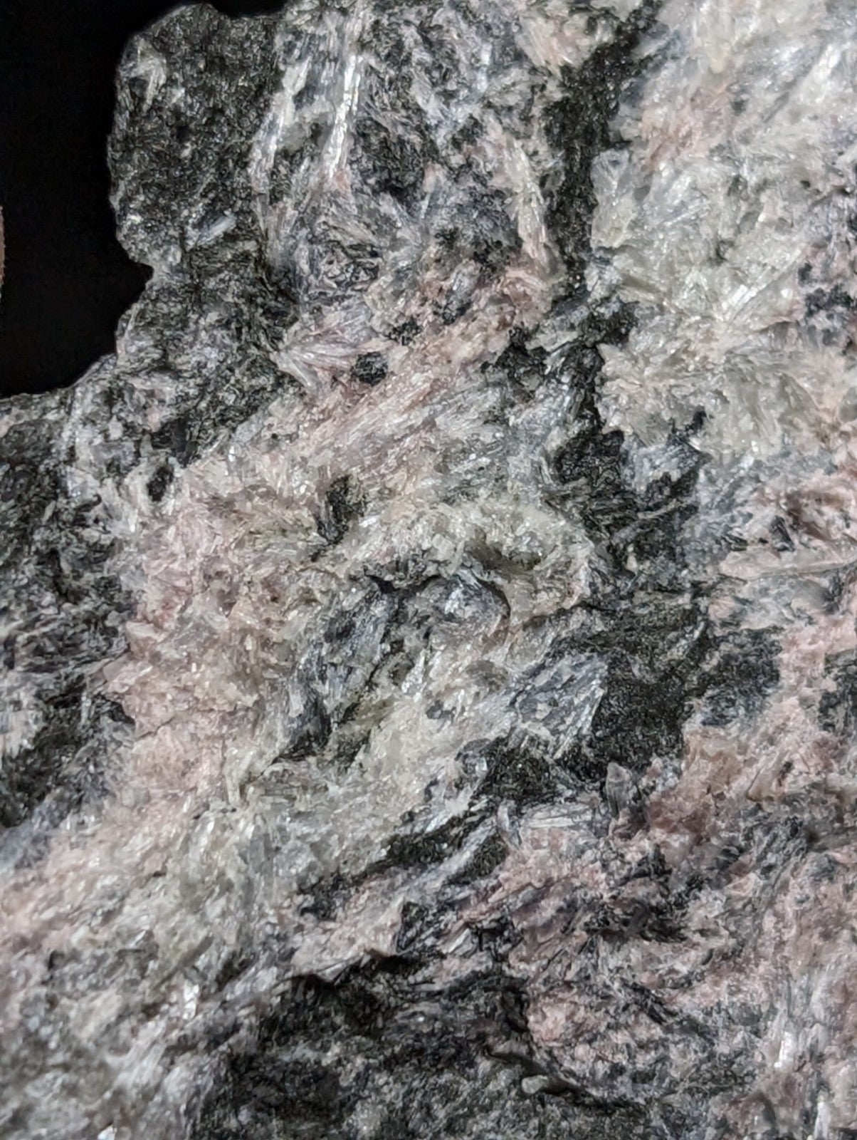 A rugged, naturally occurring rock with a mottled surface of dark gray, black, and subtle pinkish hues.
