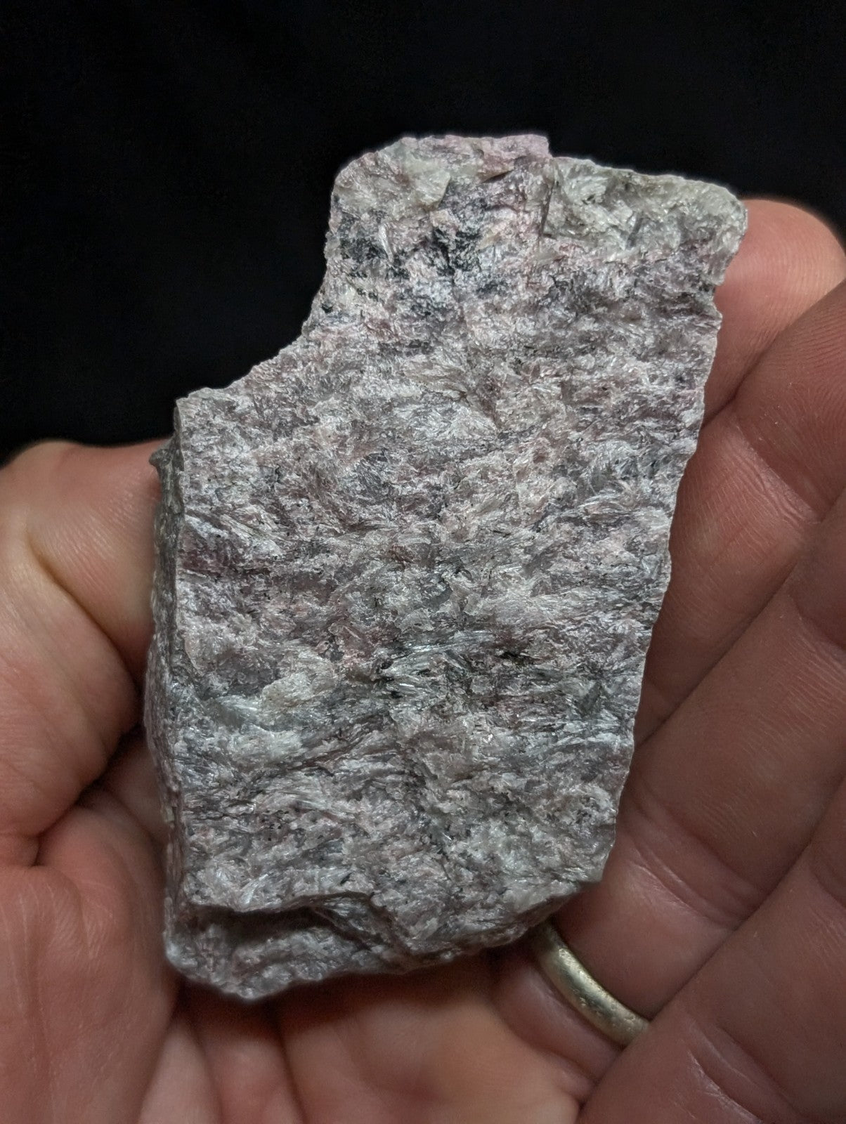 A rough, irregularly shaped gray rock with subtle pinkish hues and a textured surface held in someone’s hand.