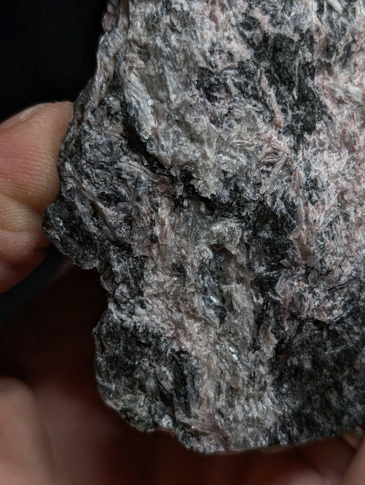 A rough, irregularly shaped rock with a mottled surface of dark gray and pinkish hues.