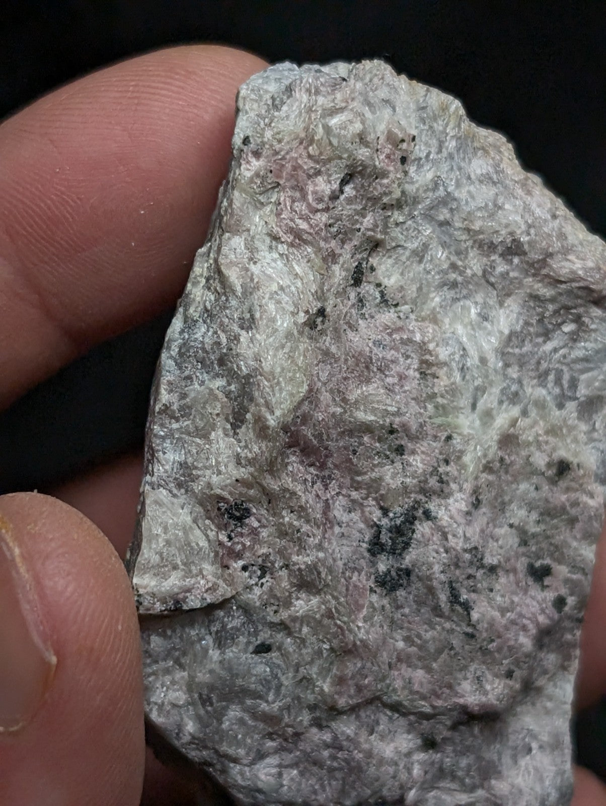 A rough, irregularly shaped stone with a mottled gray and pale pink surface, speckled with dark mineral inclusions.