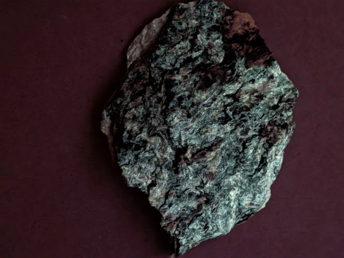 A rough, irregularly shaped piece of dark green and black speckled rock with a textured surface.