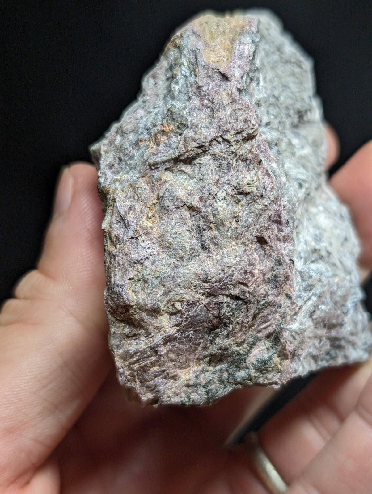 A rough, irregularly shaped stone with a mottled surface of gray, pinkish-purple, and subtle green hues.