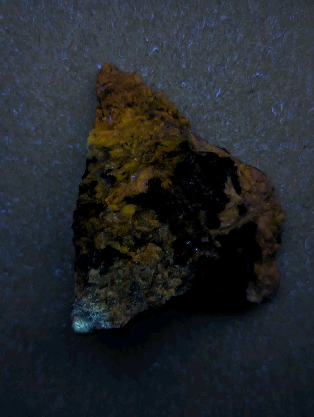 A rugged, triangular-shaped mineral specimen with a mottled surface of dark brown and vibrant yellow-orange hues.