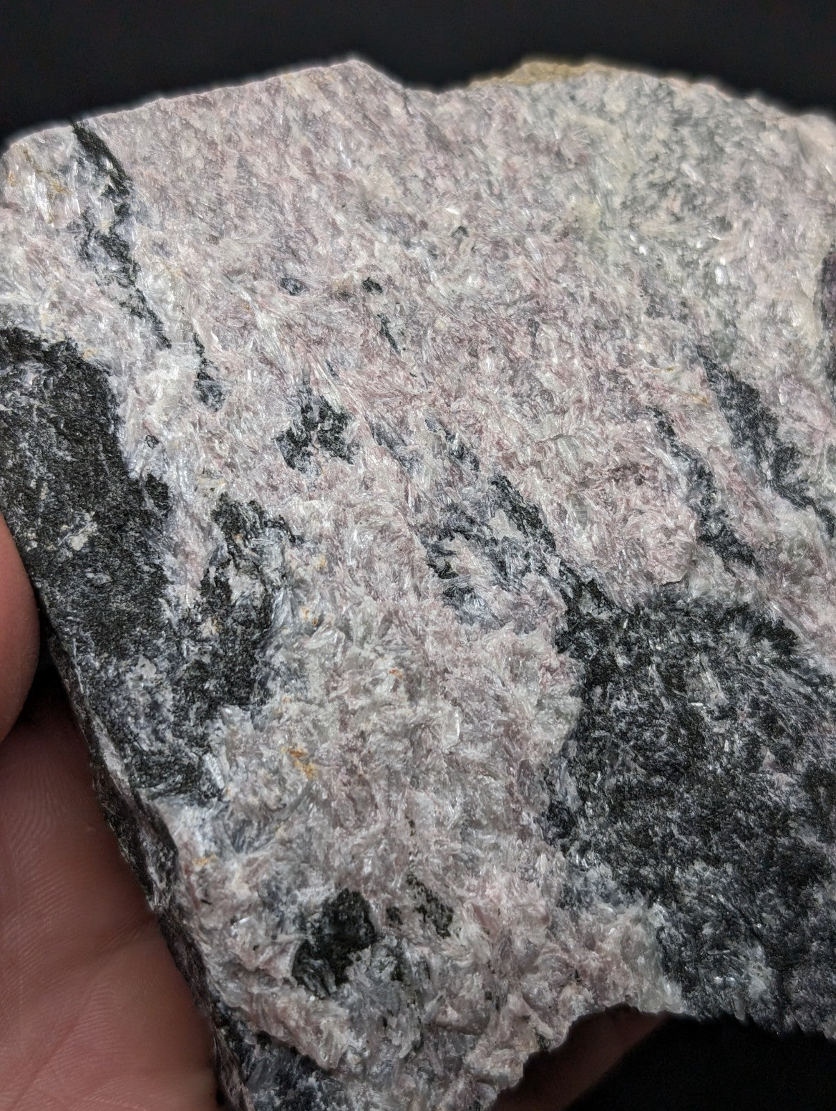 A rough, irregularly shaped rock with a mottled surface of gray and black mineral veins against a lighter pinkish-gray base.