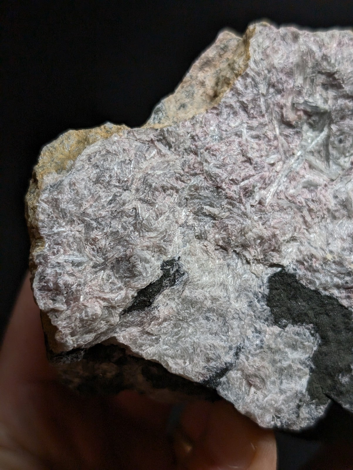 A rough, irregularly shaped mineral specimen with a textured surface displaying silvery-white crystalline fibers embedded in a pale pinkish-gray matrix.