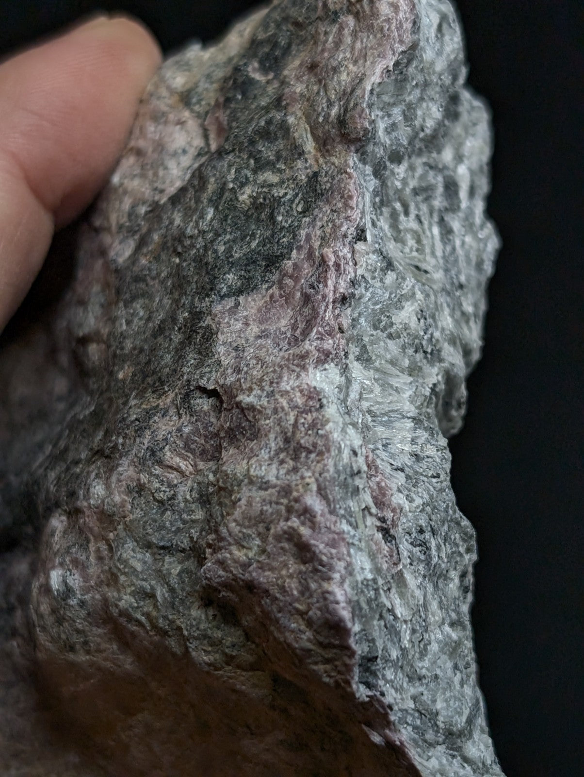 A rugged, naturally textured rock with a mottled pattern of gray, green, and subtle pinkish hues.