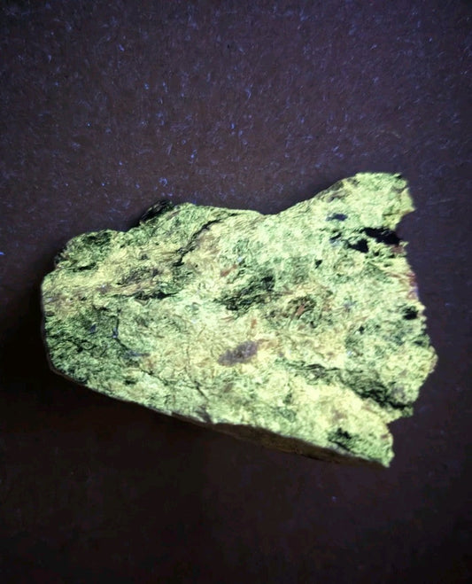 A rough, irregularly shaped piece of greenish-yellow mineral with dark speckles and a textured surface.