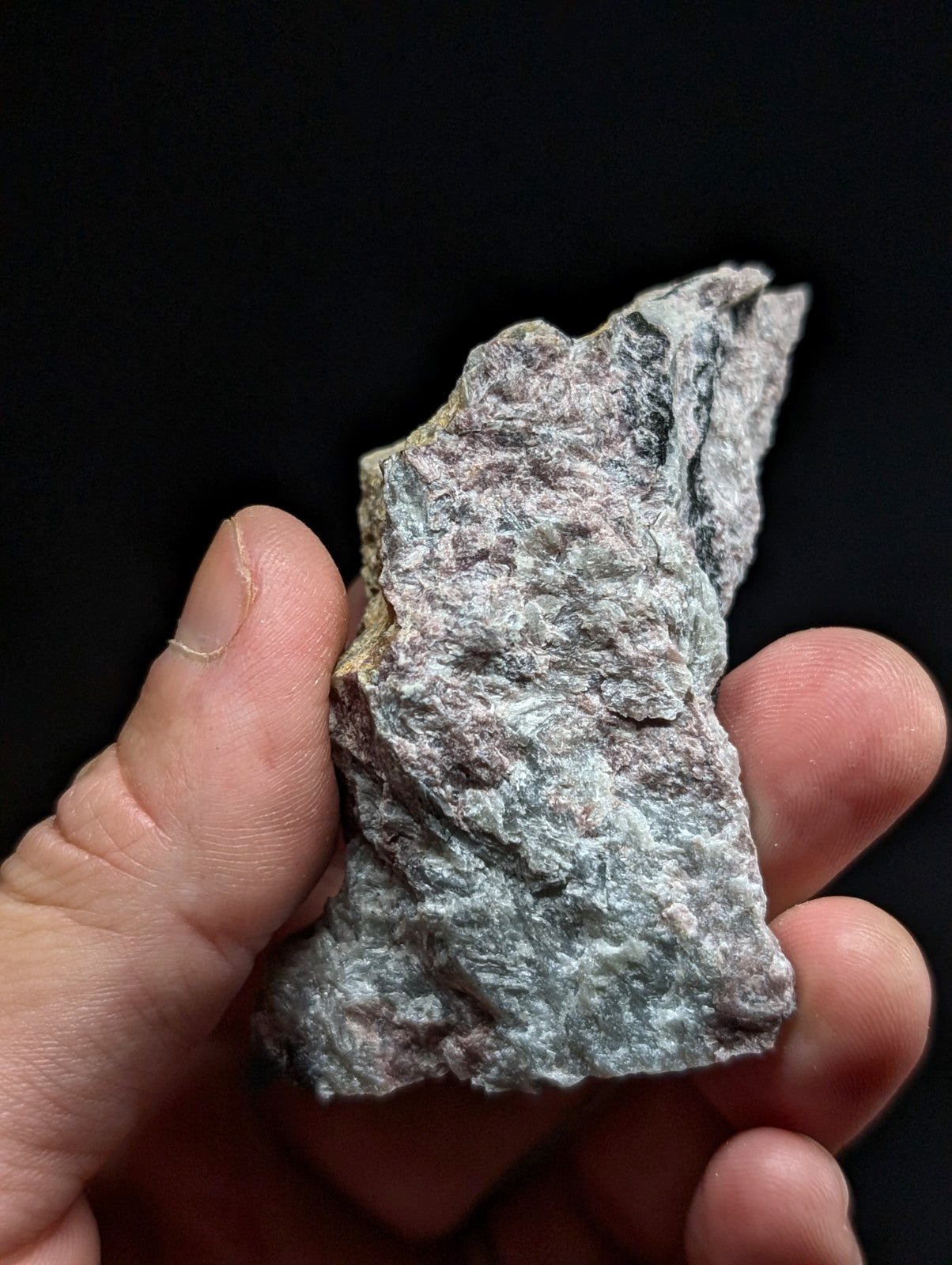 A rough, irregularly shaped piece of grayish-green stone with a textured surface and subtle pinkish undertones.