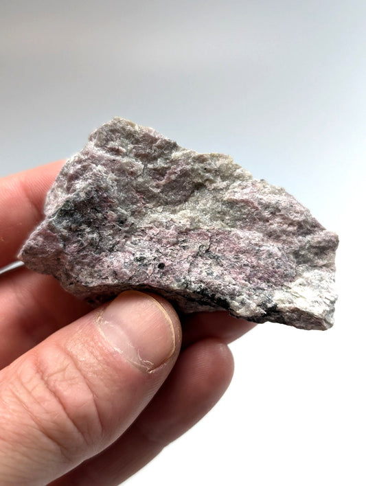 A rough, irregularly shaped piece of grayish-purple rock with speckled black and white patches.