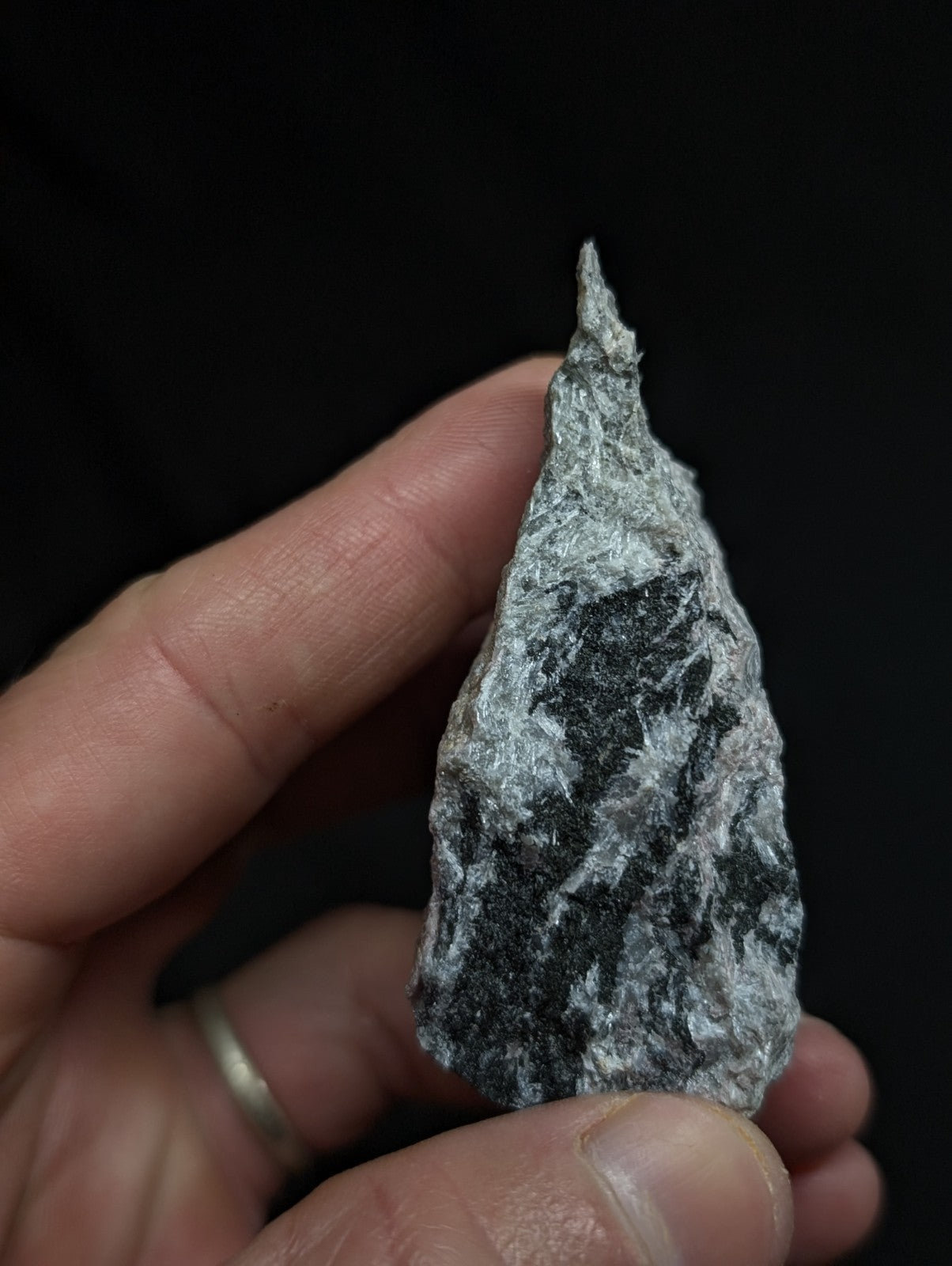 A hand holds a gray and black speckled stone with a pointed, irregularly shaped tip.