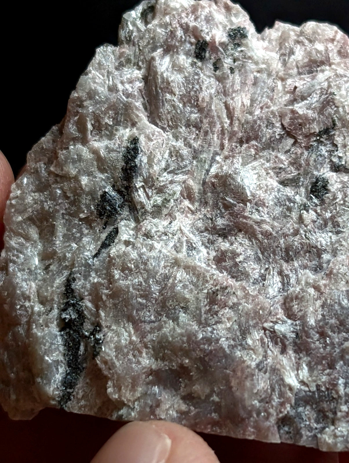 A rough, pale pinkish-gray mineral specimen with dark black streaks and a crystalline texture.