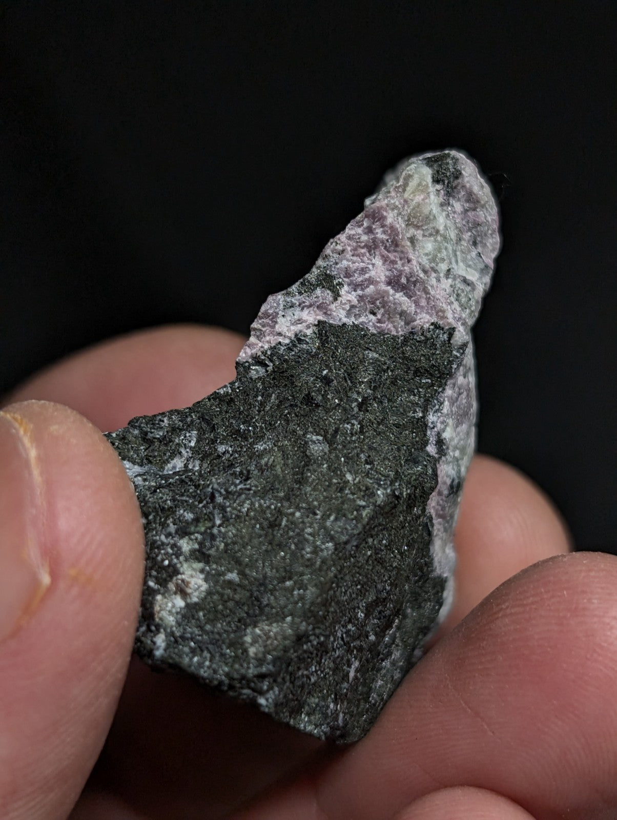 A rough, irregularly shaped mineral specimen with a dark gray base and patches of lighter purple and white veining.
