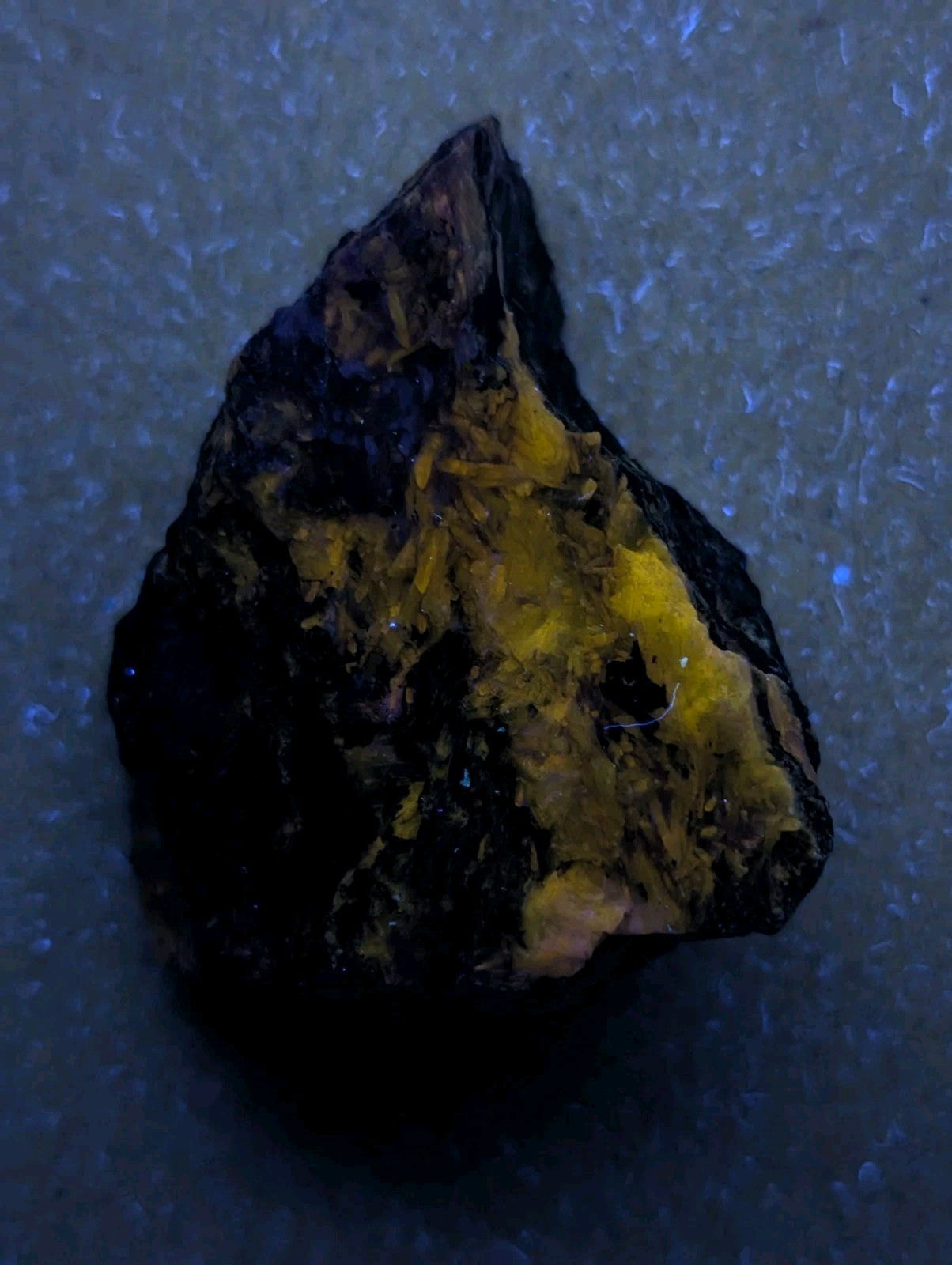 A rugged, irregularly shaped mineral specimen with a dark, almost black exterior and vibrant yellow crystalline inclusions.