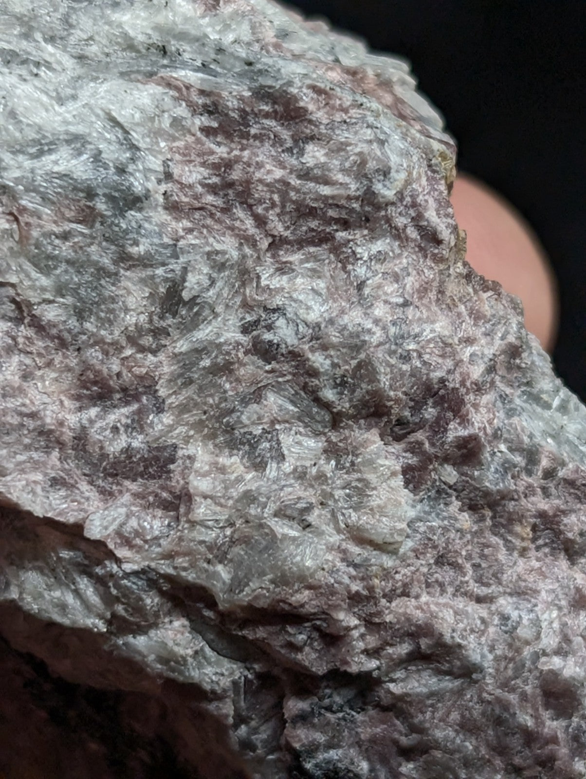A rough, textured mineral specimen with a mottled gray and pinkish hue.
