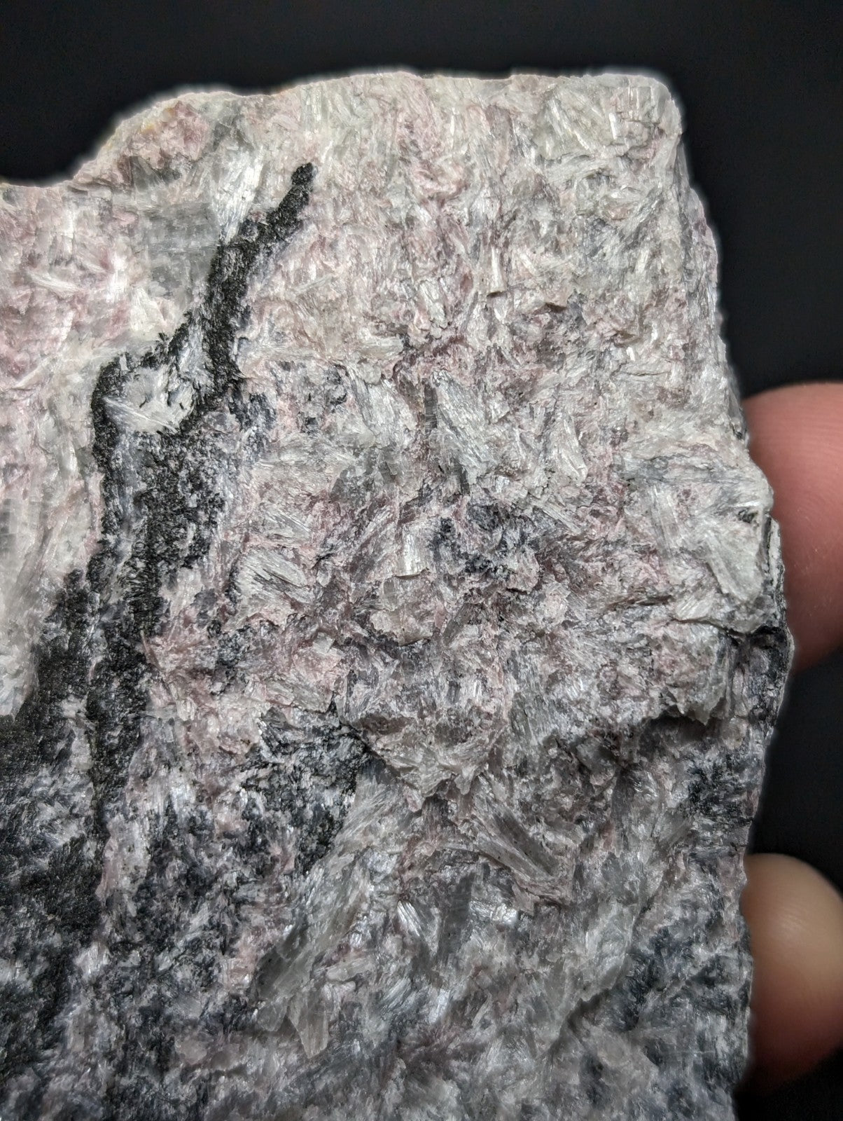 A rough, irregularly shaped piece of mineral with a mottled gray and pinkish surface featuring prominent dark streaks.