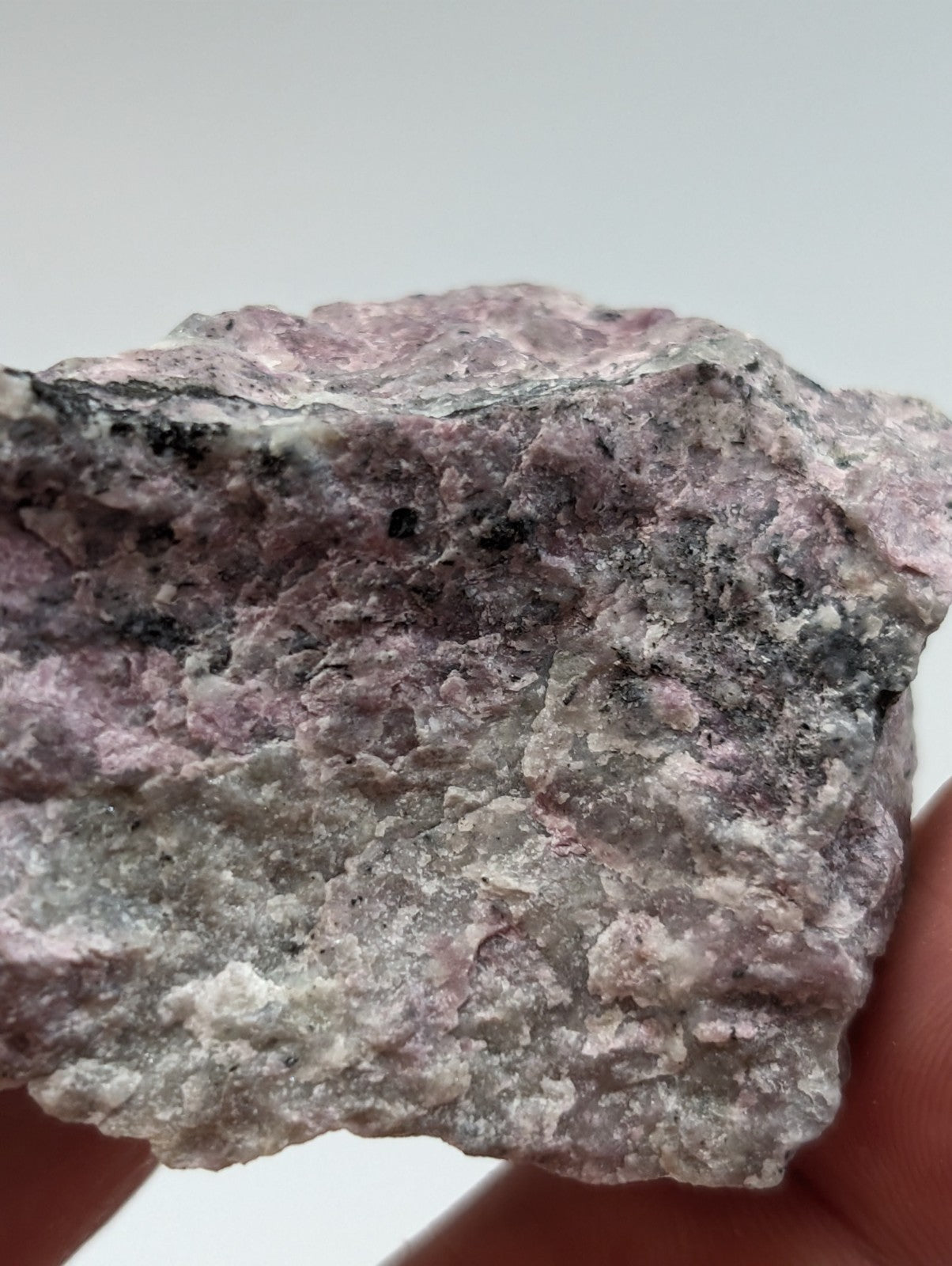 A rough, irregularly shaped piece of pink and gray mineral rock with speckled black inclusions.