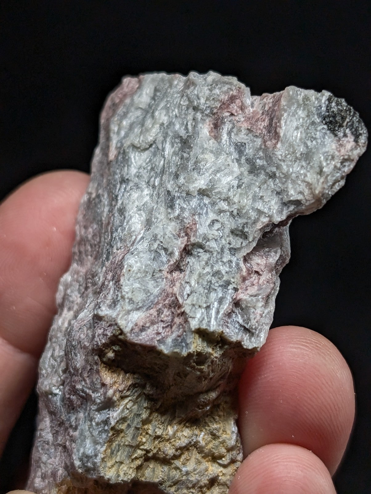 A rough, irregularly shaped mineral specimen with a mottled gray surface accented by patches of pink and yellowish hues.