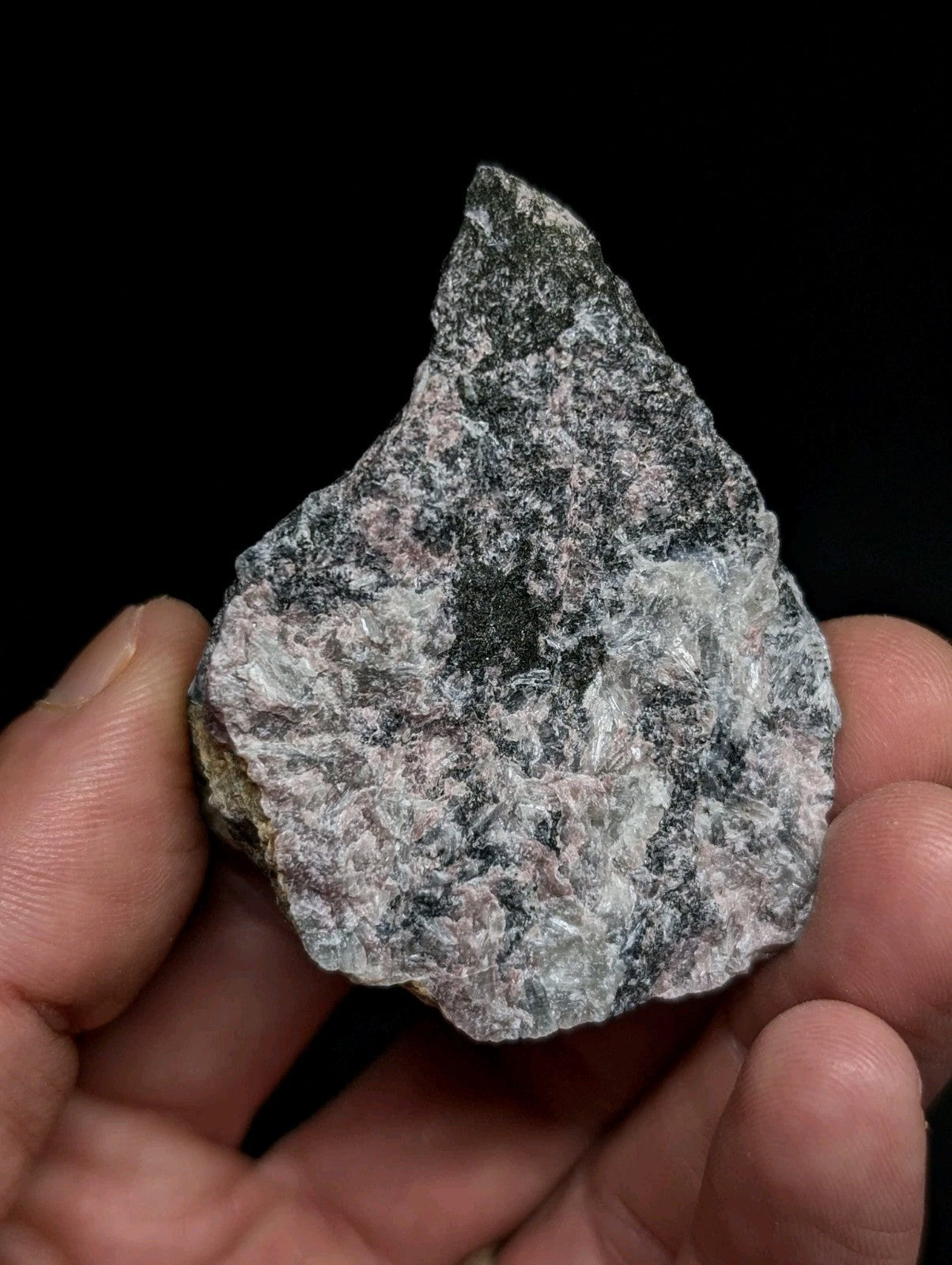 A rough, irregularly shaped stone with a mottled pattern of gray, black, and subtle pinkish hues.